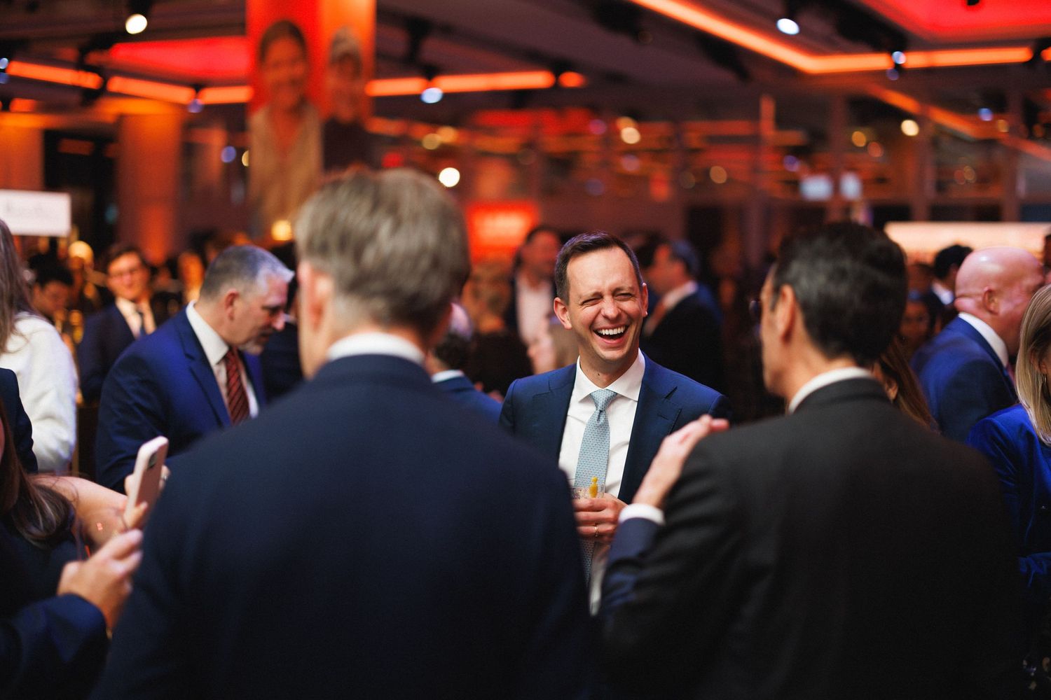 People mingling and socializing at an indoor evening event with red ambient lighting.