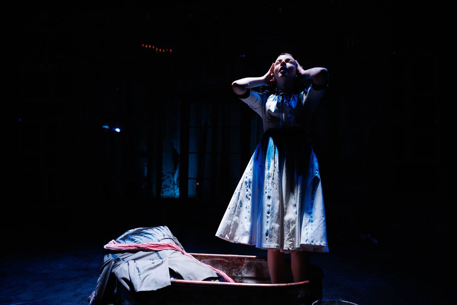 Dramatic stage performance featuring a figure in a flowing dress under theatrical lighting.