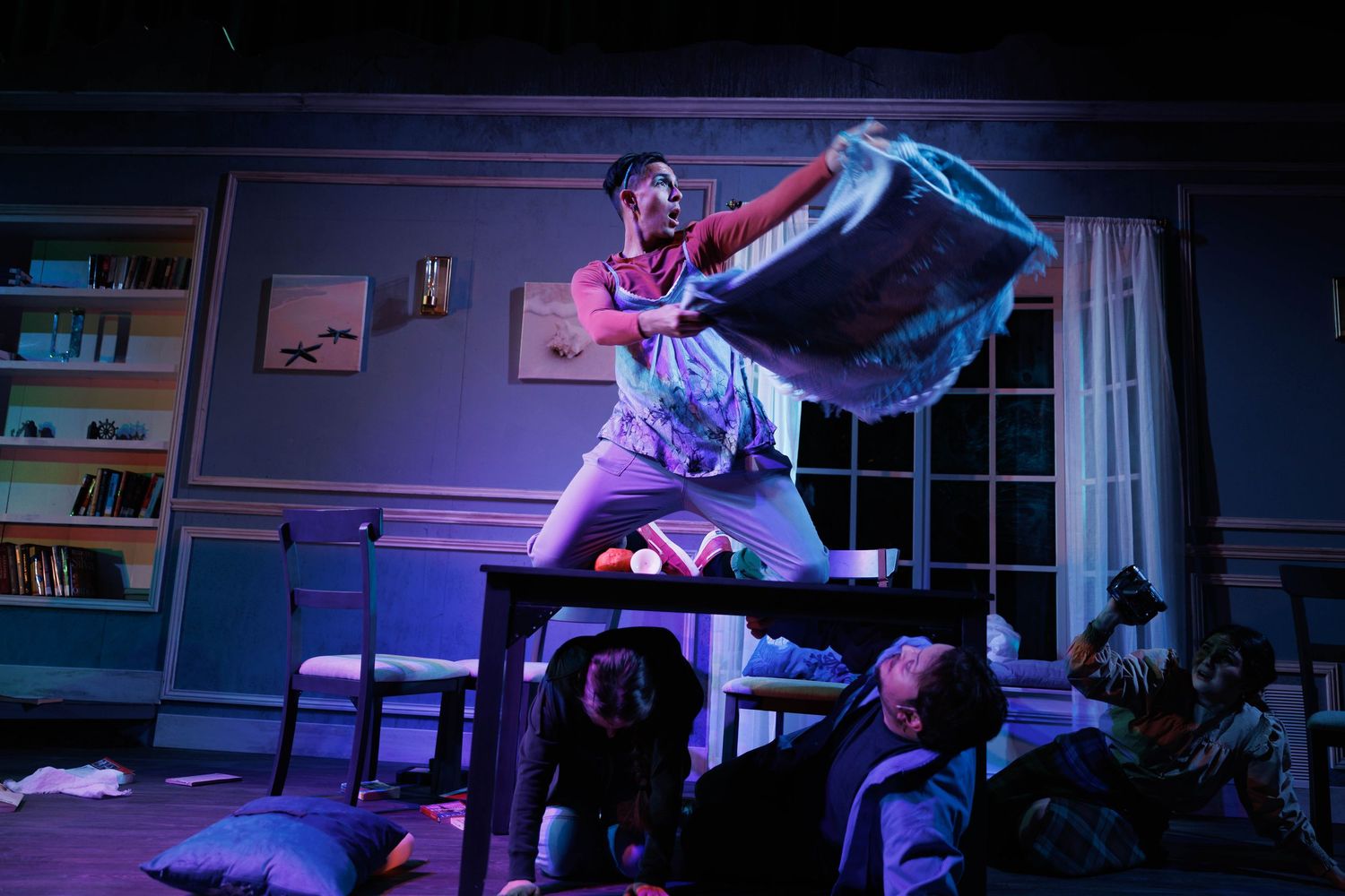 A person in sleepwear jumps on a bed while holding a blanket, illuminated by dramatic purple and blue lighting.