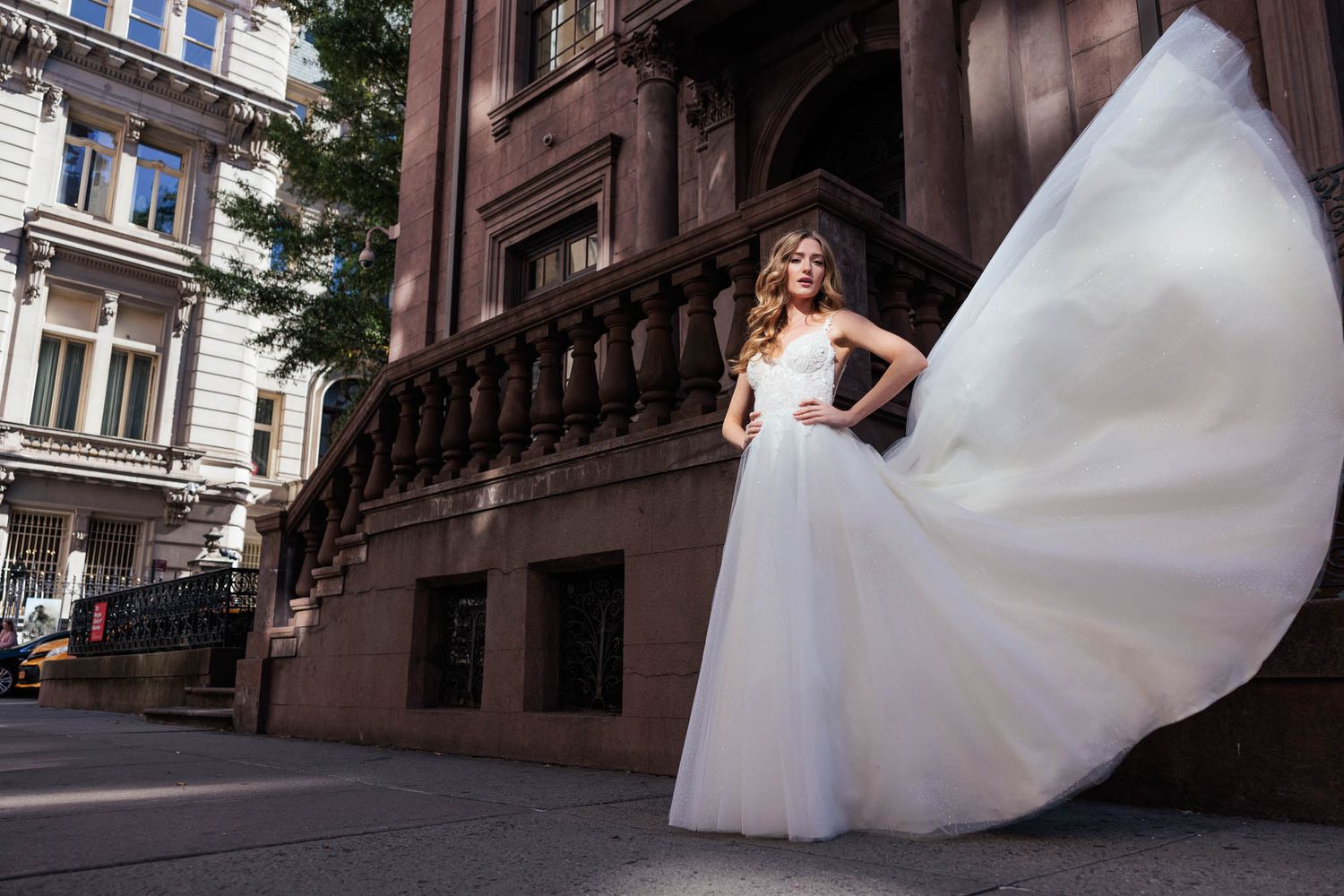 Bride in flowing white dress twirling on historic European-style street.