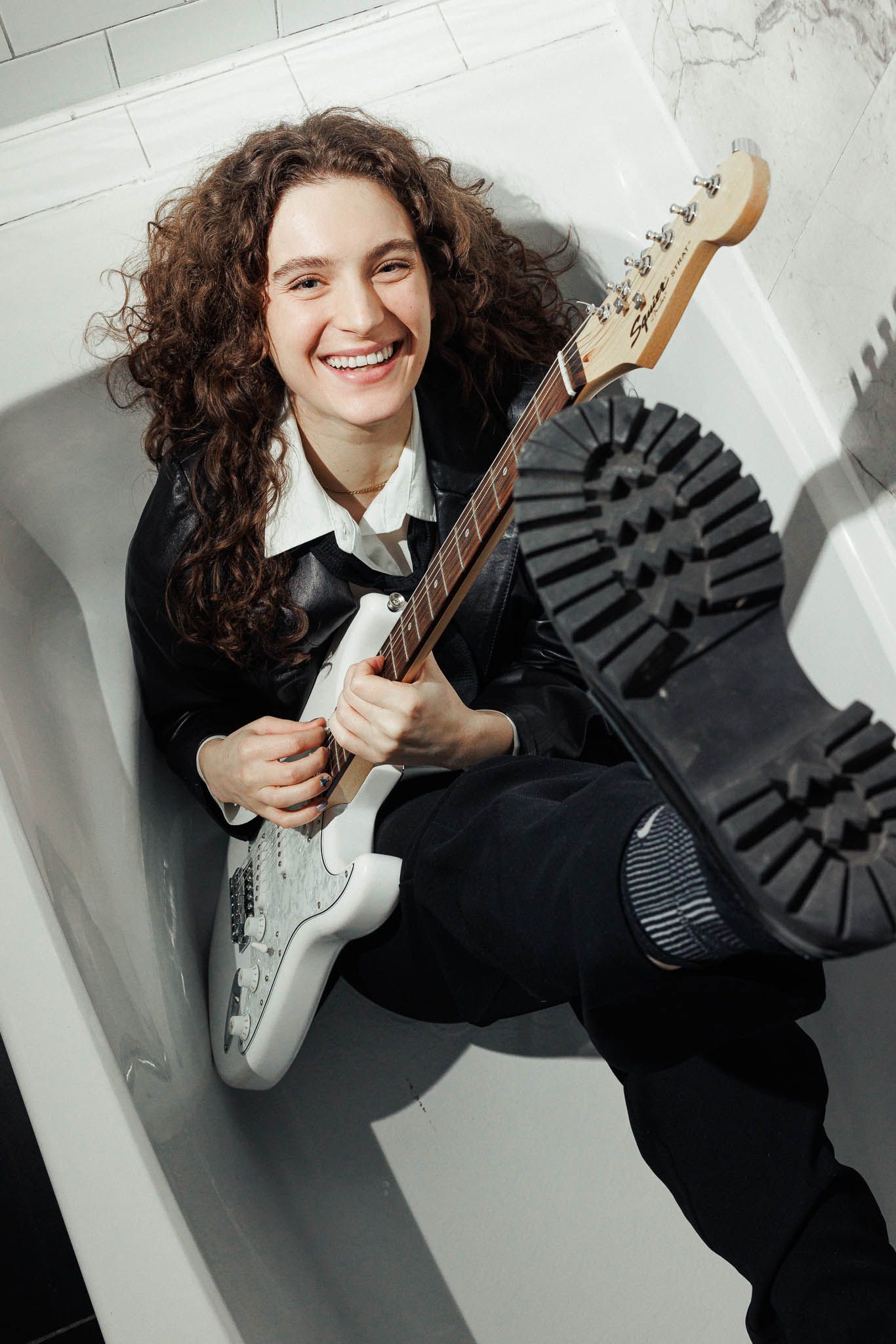 Multiple shots of musician playing electric guitar in black attire in a white bathtub.