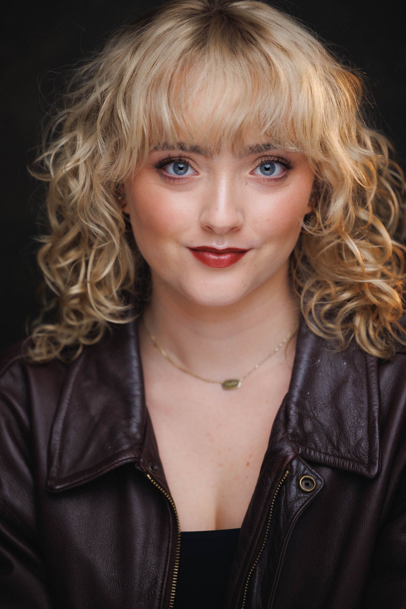 Professional headshot series of someone with curly blonde hair and red lipstick wearing a black leather jacket against dark background.