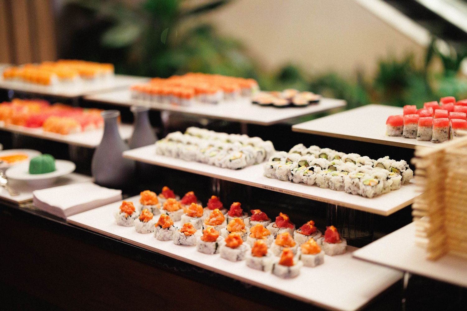 Rows of colorful sushi rolls and appetizers displayed on white serving platters at an upscale restaurant buffet.