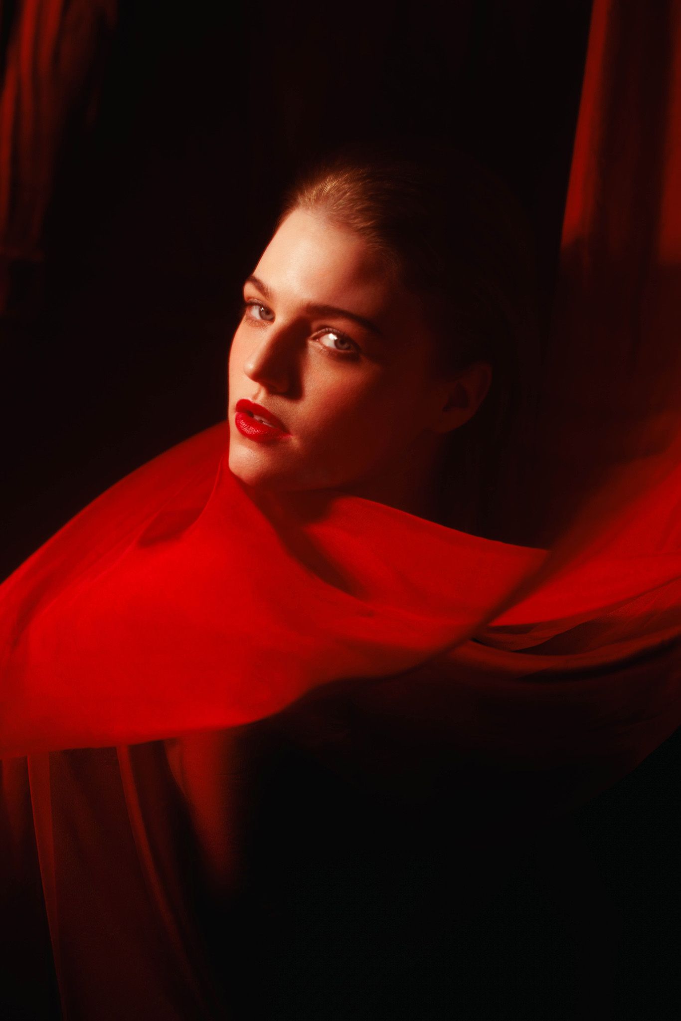 Artistic portrait with red lighting and fabric creating a dramatic atmosphere.