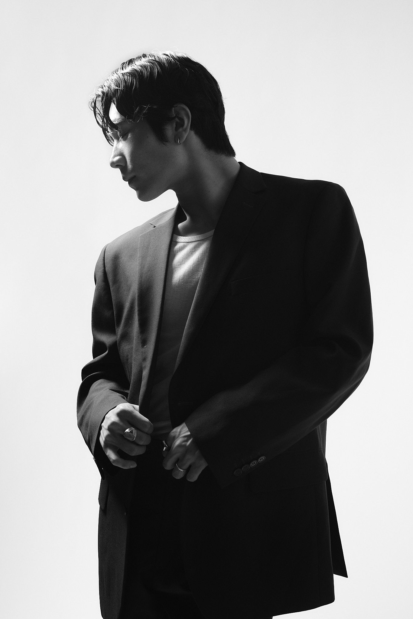 Black and white portrait of a man in a dark blazer looking sideways, dramatic lighting against white background.