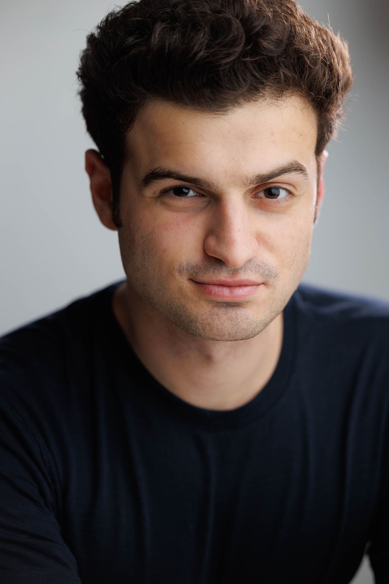 Professional headshot portrait of a person wearing a dark shirt against a light background.