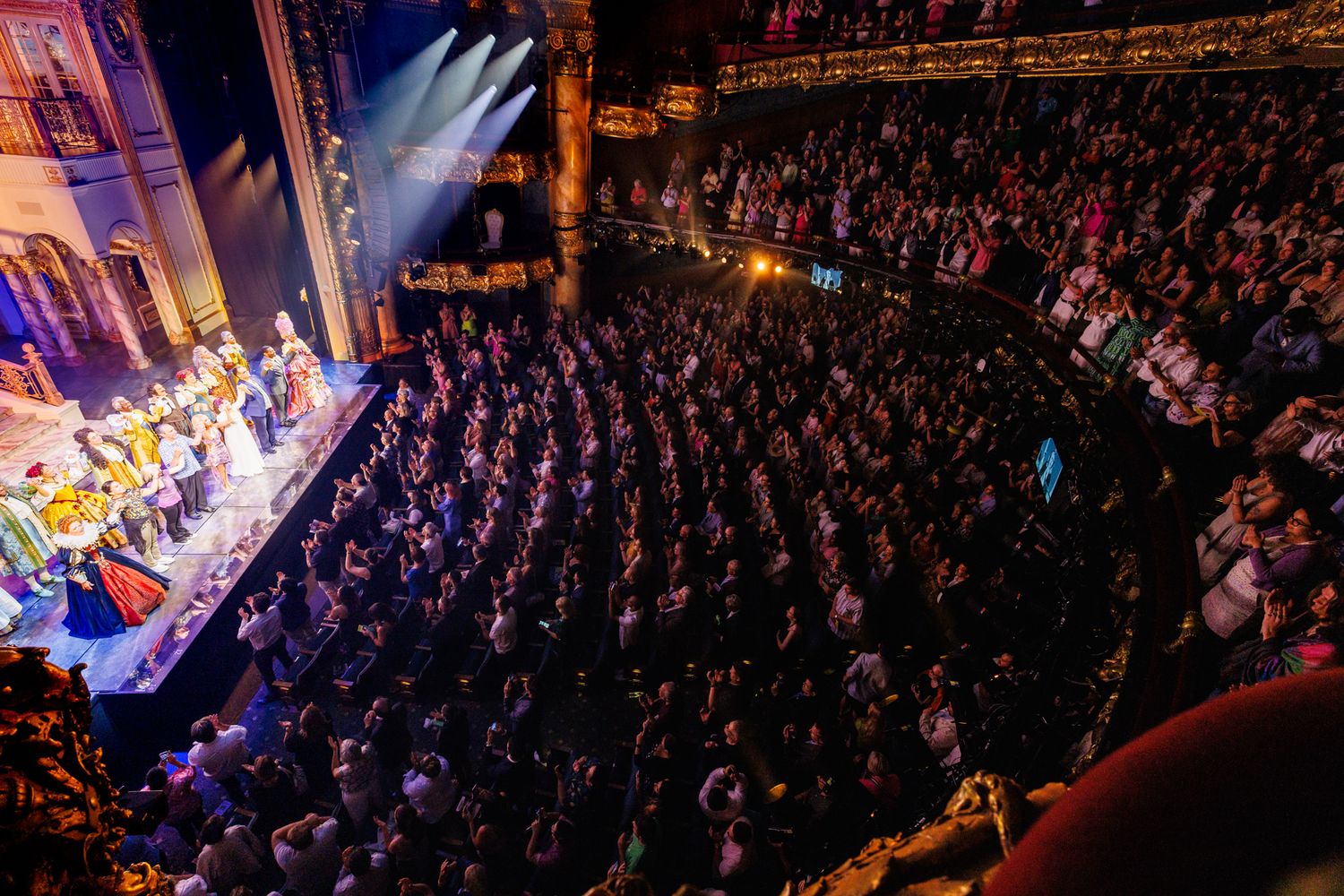 Packed theater audience watching a vibrant stage performance with colorful lighting.