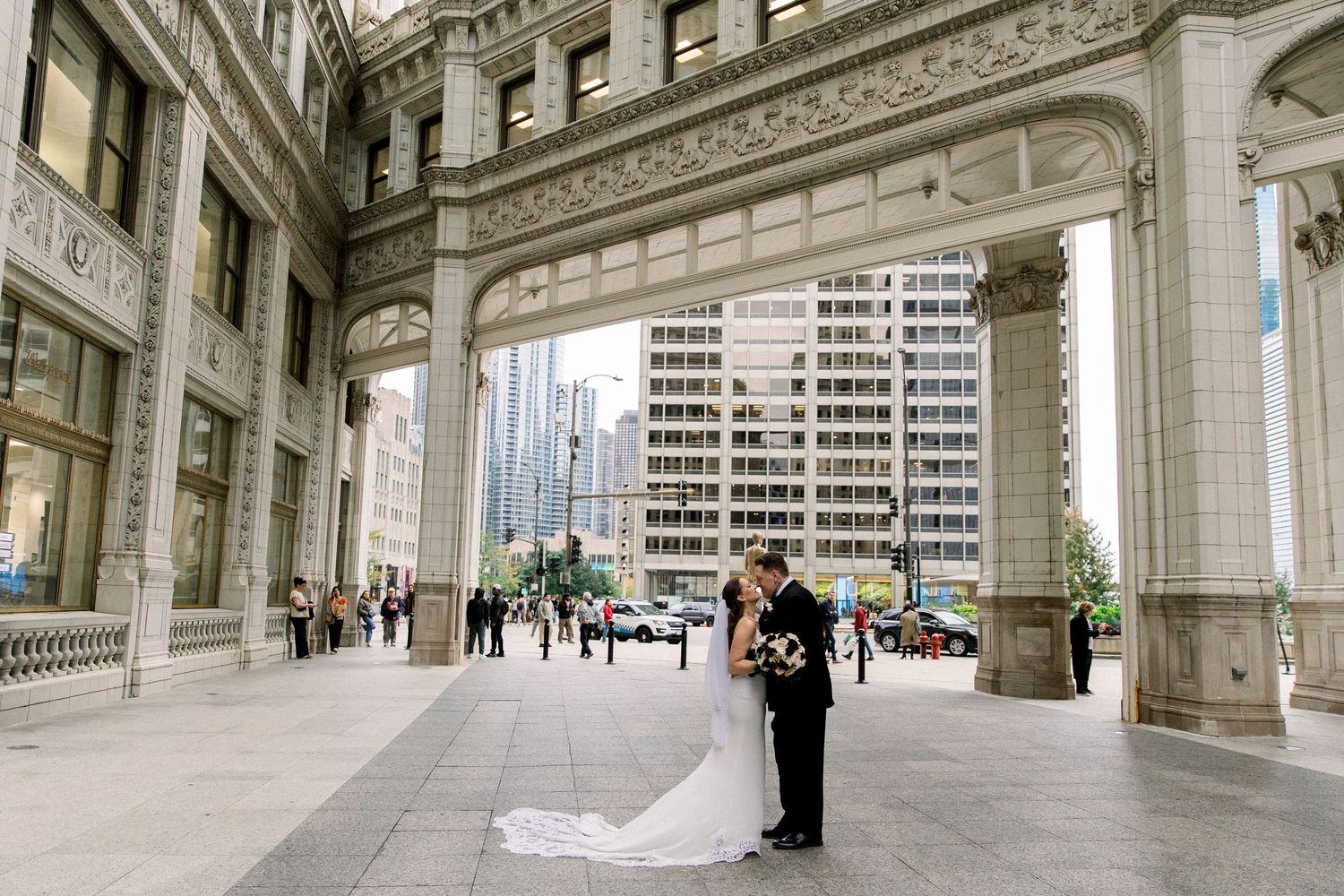 Bride and groom share a romantic kiss under ornate stone arches of a grand Chicago building on their wedding day.