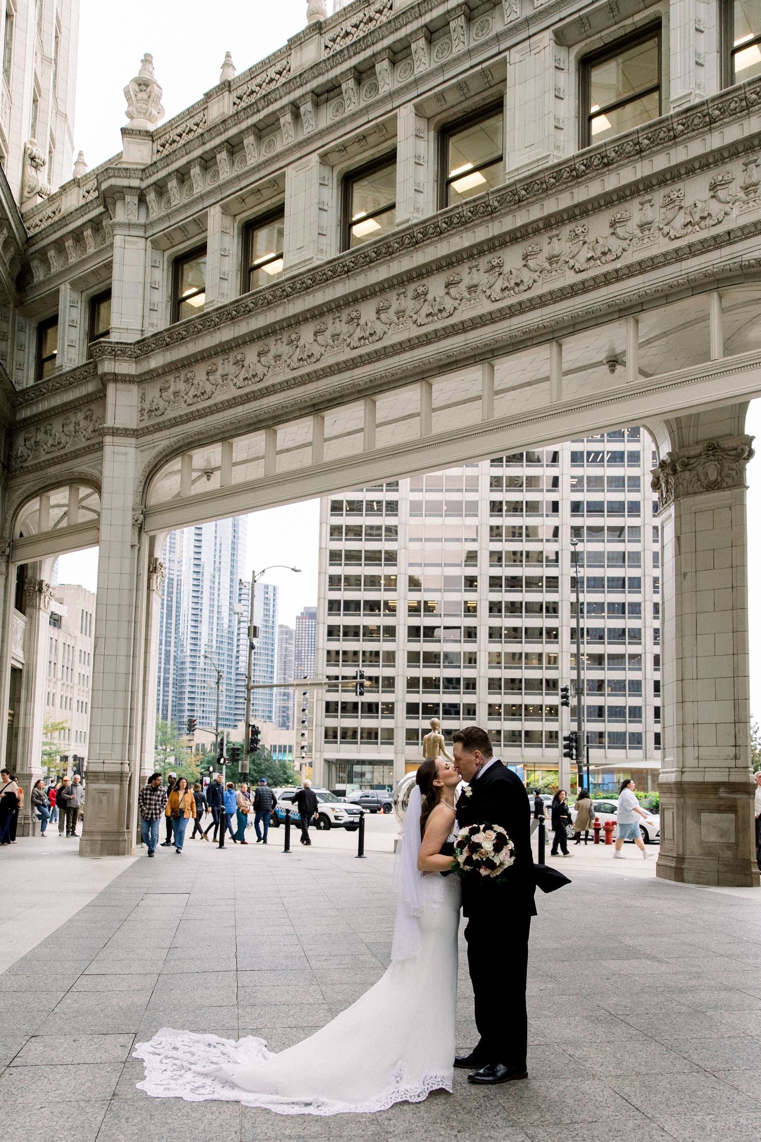 Bride and groom share romantic kiss under ornate stone arch bridge on Michigan Avenue in downtown Chicago.