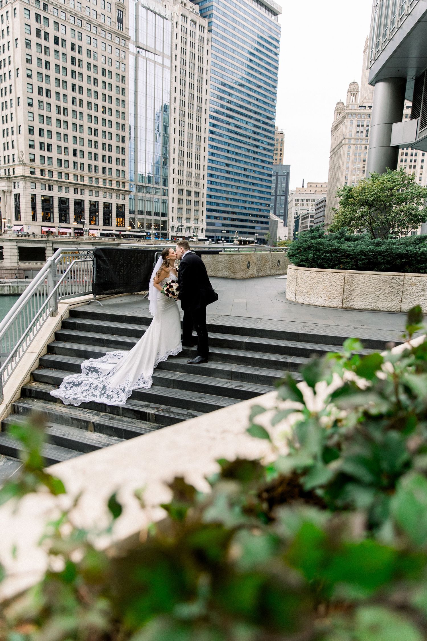 Bride and groom sharing romantic kiss on steps with Chicago city skyline in background.