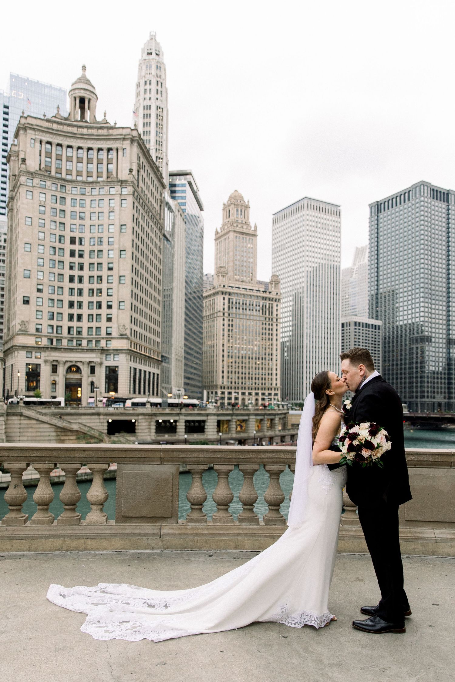 Bride and groom kissing on bridge with Chicago skyline skyscrapers in background.