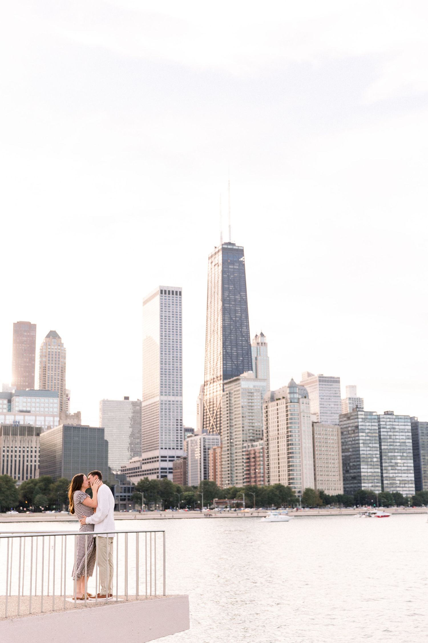 Couple kissing on a pier with Chicago skyline and John Hancock Center in the background.
