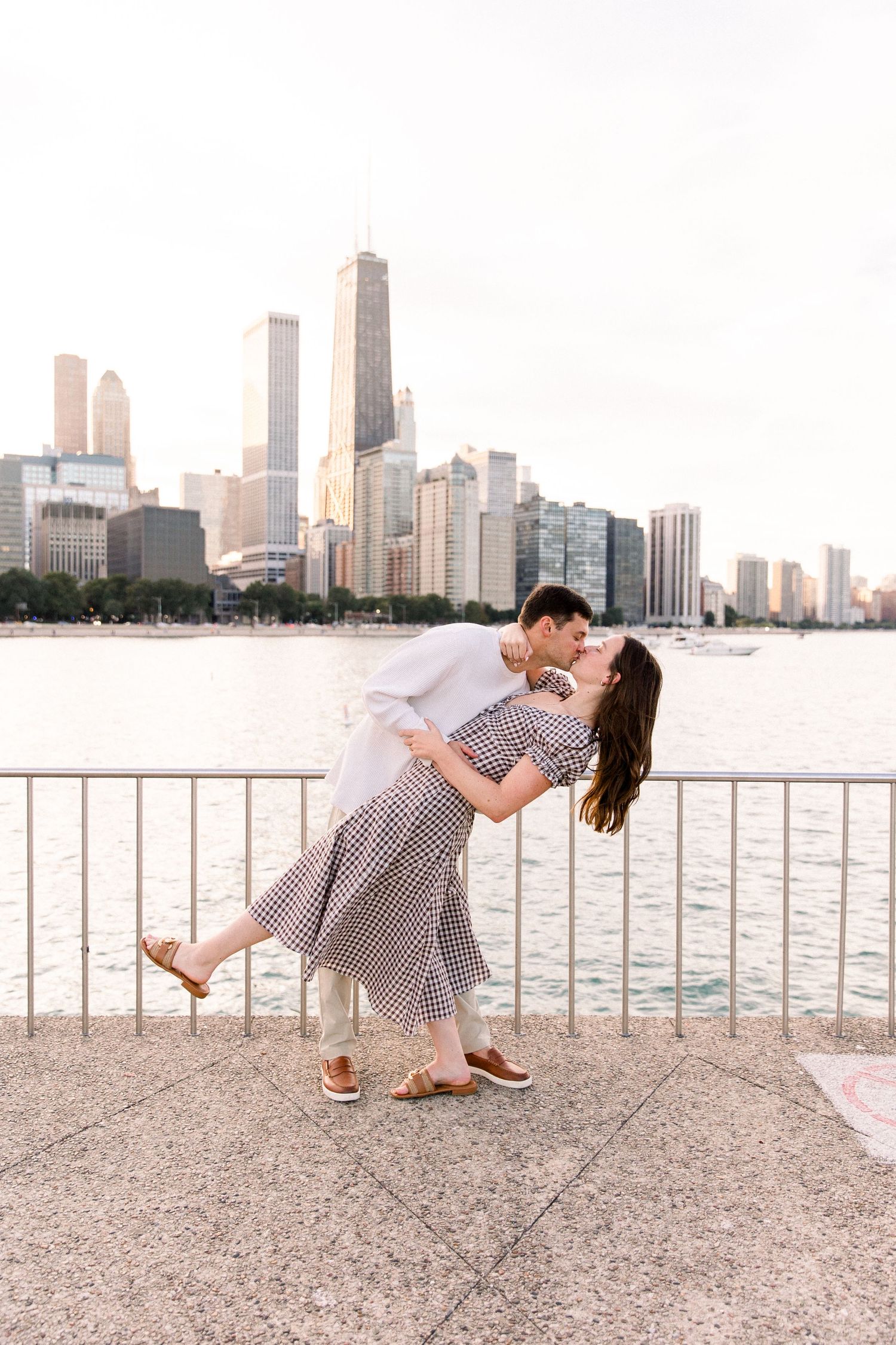 Couple sharing a romantic dip kiss on Chicago lakefront with city skyline and John Hancock tower in background.