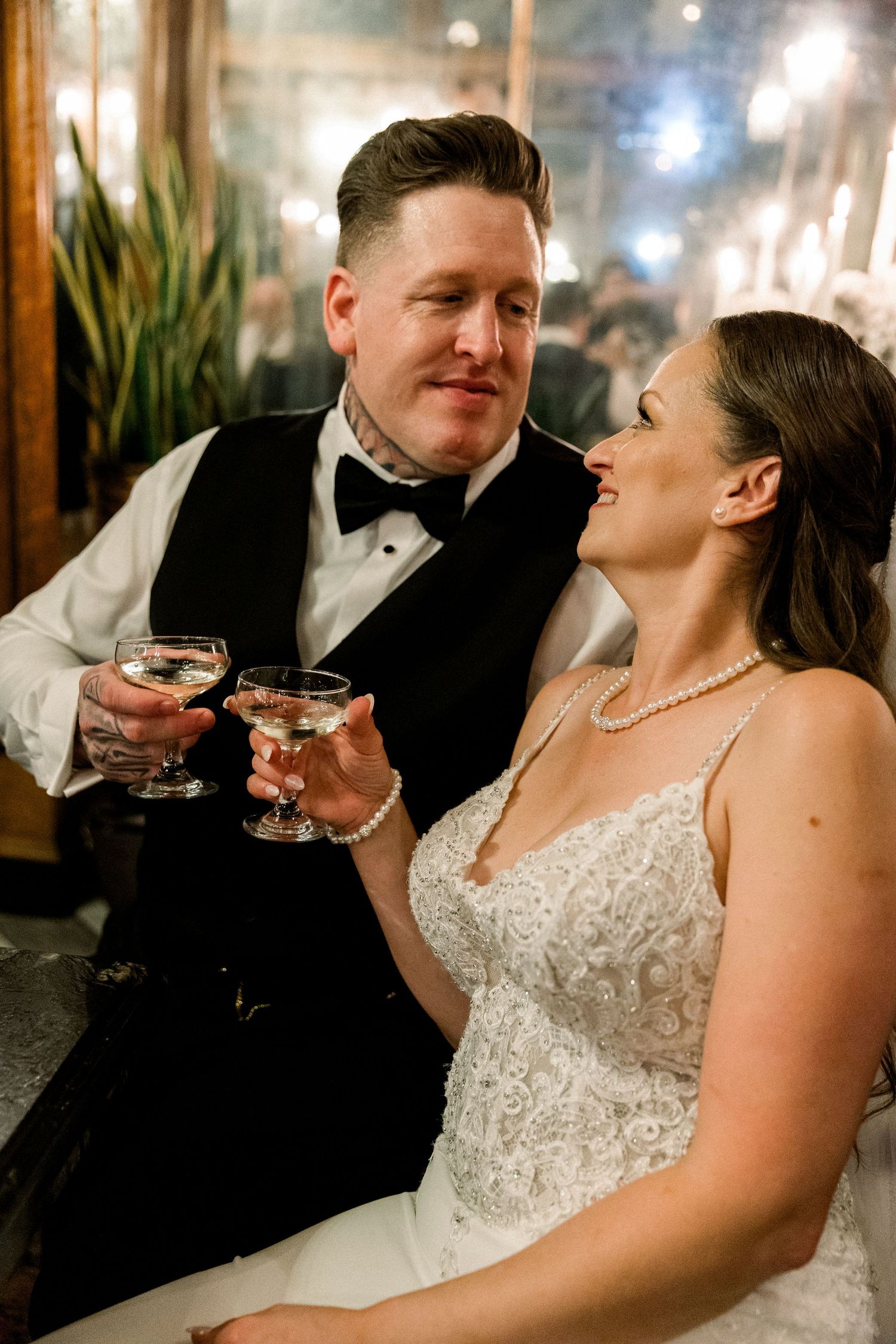 Newlyweds toasting with cocktail glasses and smiling at each other during wedding reception.