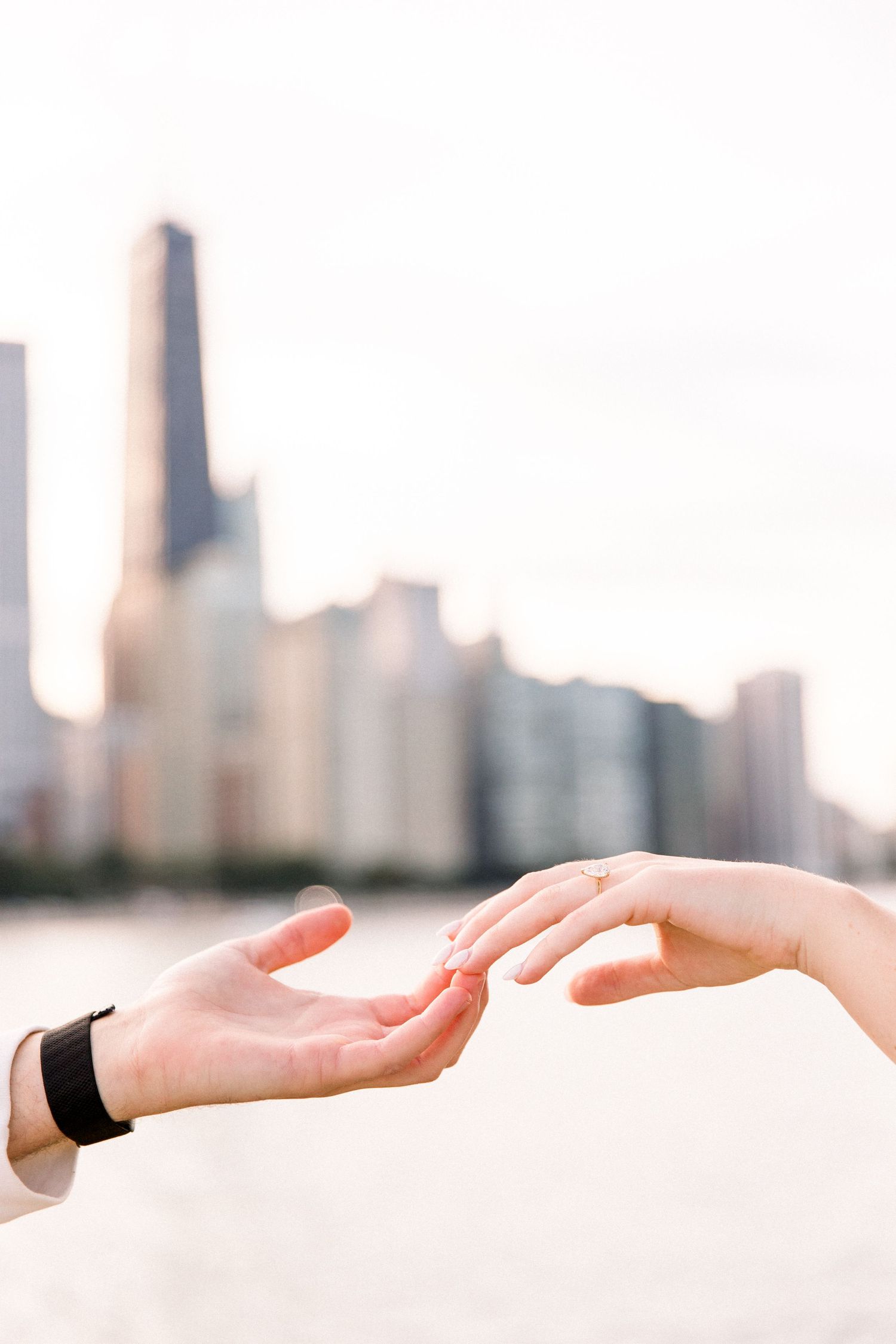Two hands reaching toward each other with blurred Chicago skyline and waterfront in the background.