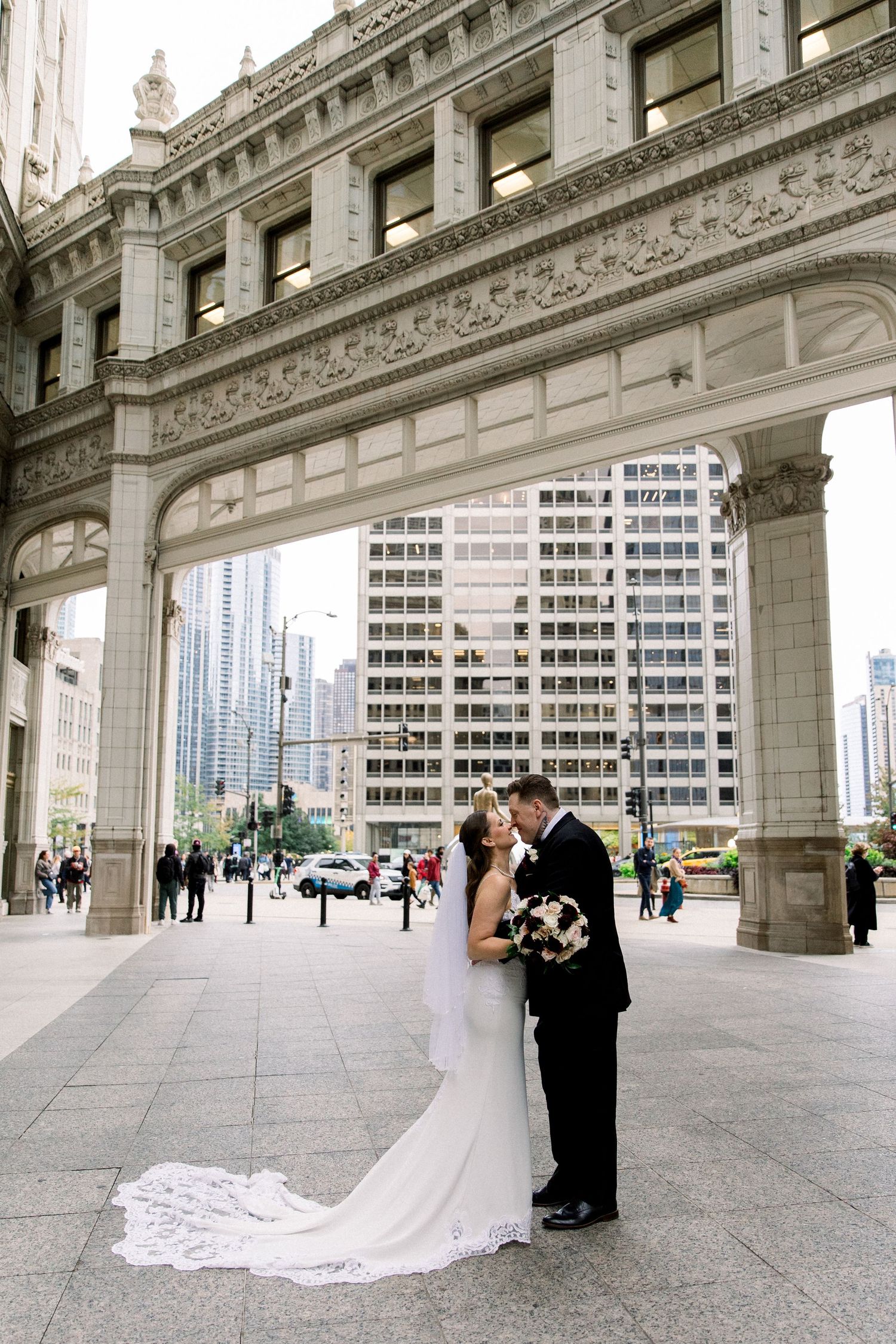 Bride and groom share a romantic kiss under an ornate stone arch on Michigan Avenue in Chicago.