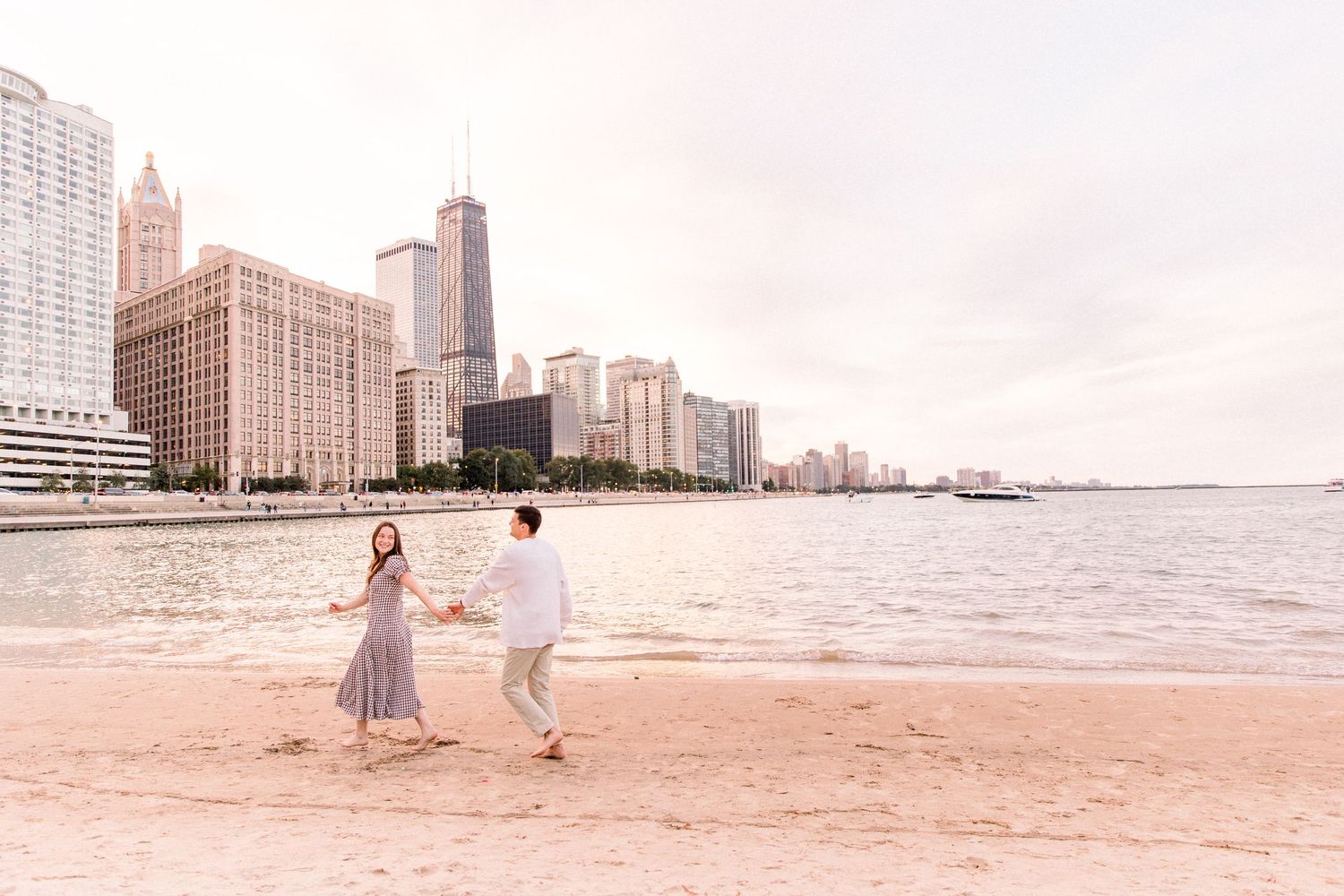 Couple holding hands and dancing on a sandy Chicago beach with the city skyline and lake in the background.