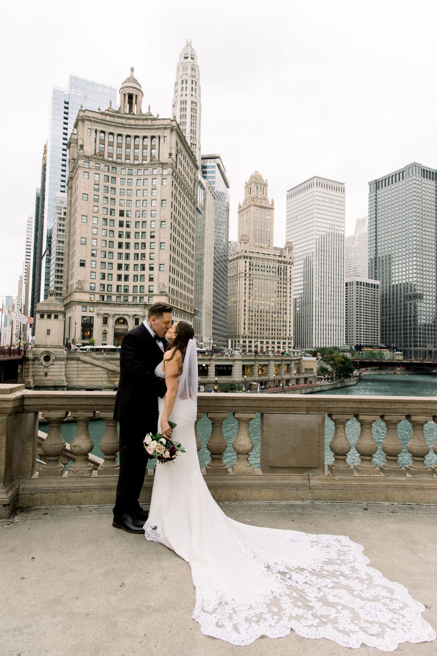 Bride and groom share a romantic kiss on a bridge with Chicago skyline and river in the background.