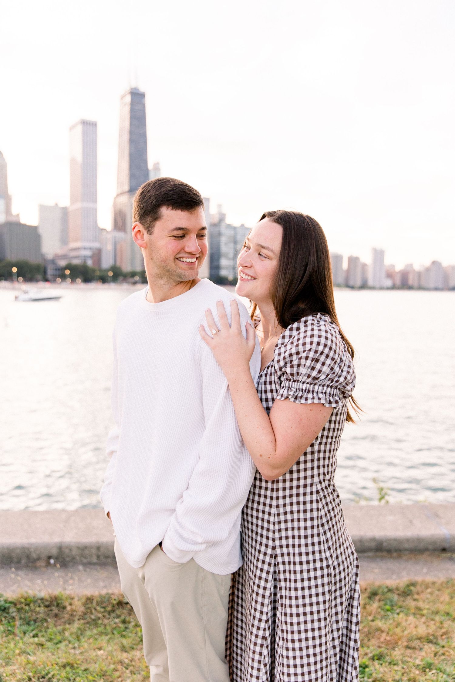 Happy couple embracing and smiling by Lake Michigan with Chicago skyline in the background.