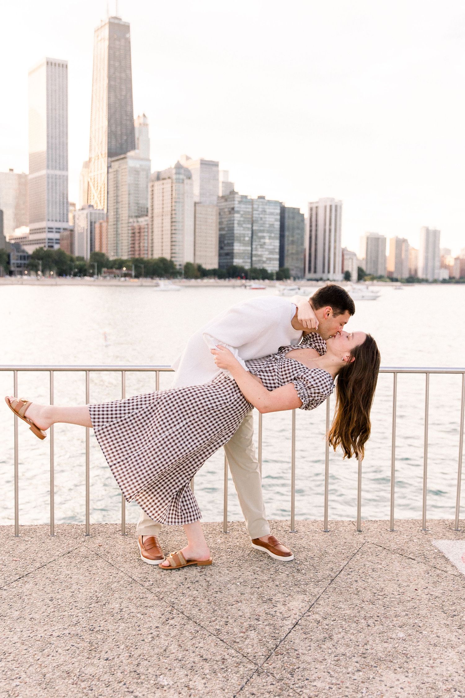Couple sharing a romantic dip kiss on Chicago waterfront with city skyline backdrop at golden hour.
