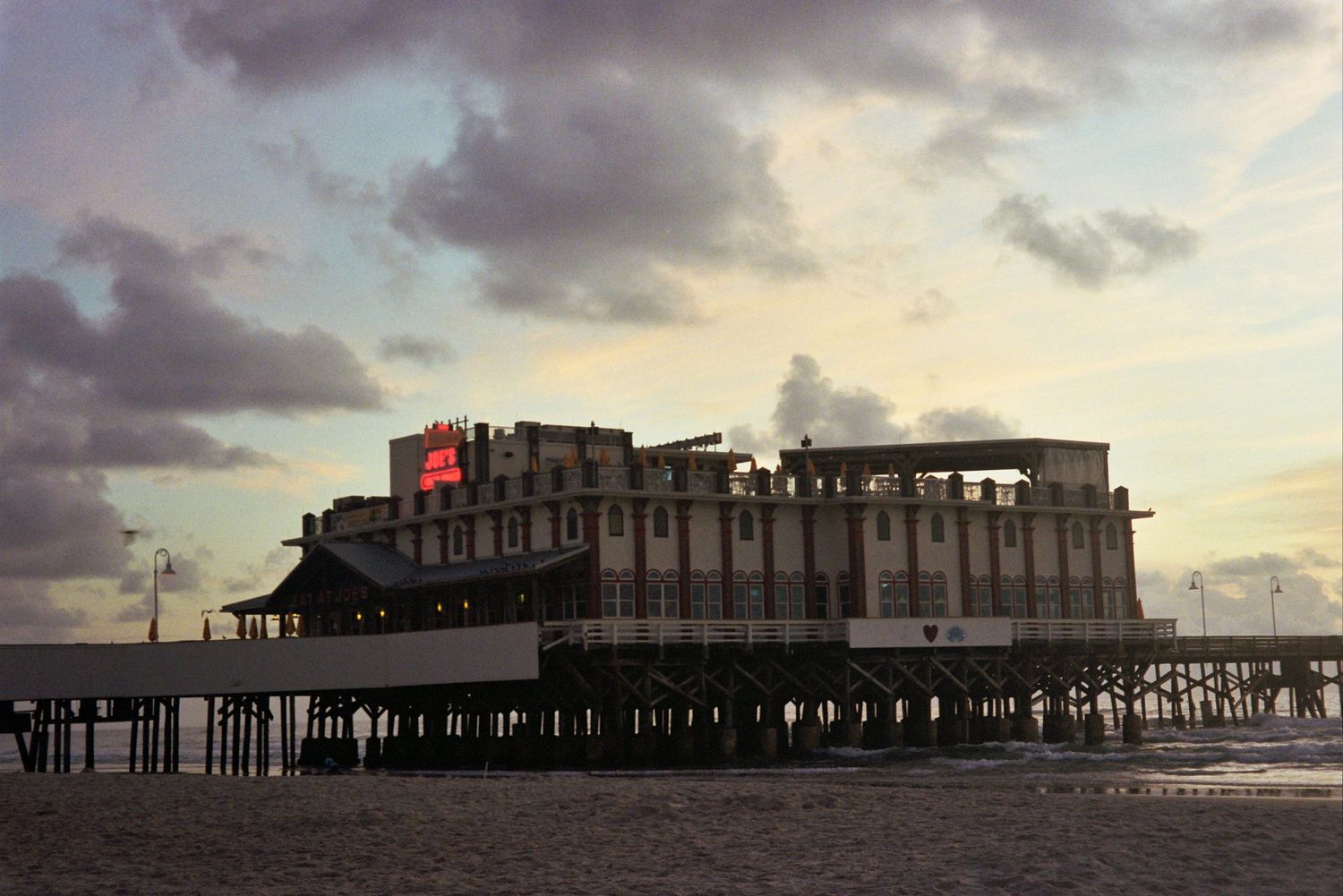 Silhouette of Joe's Crab Shack at sunrise against dramatic cloudy sky in Daytona Beach.