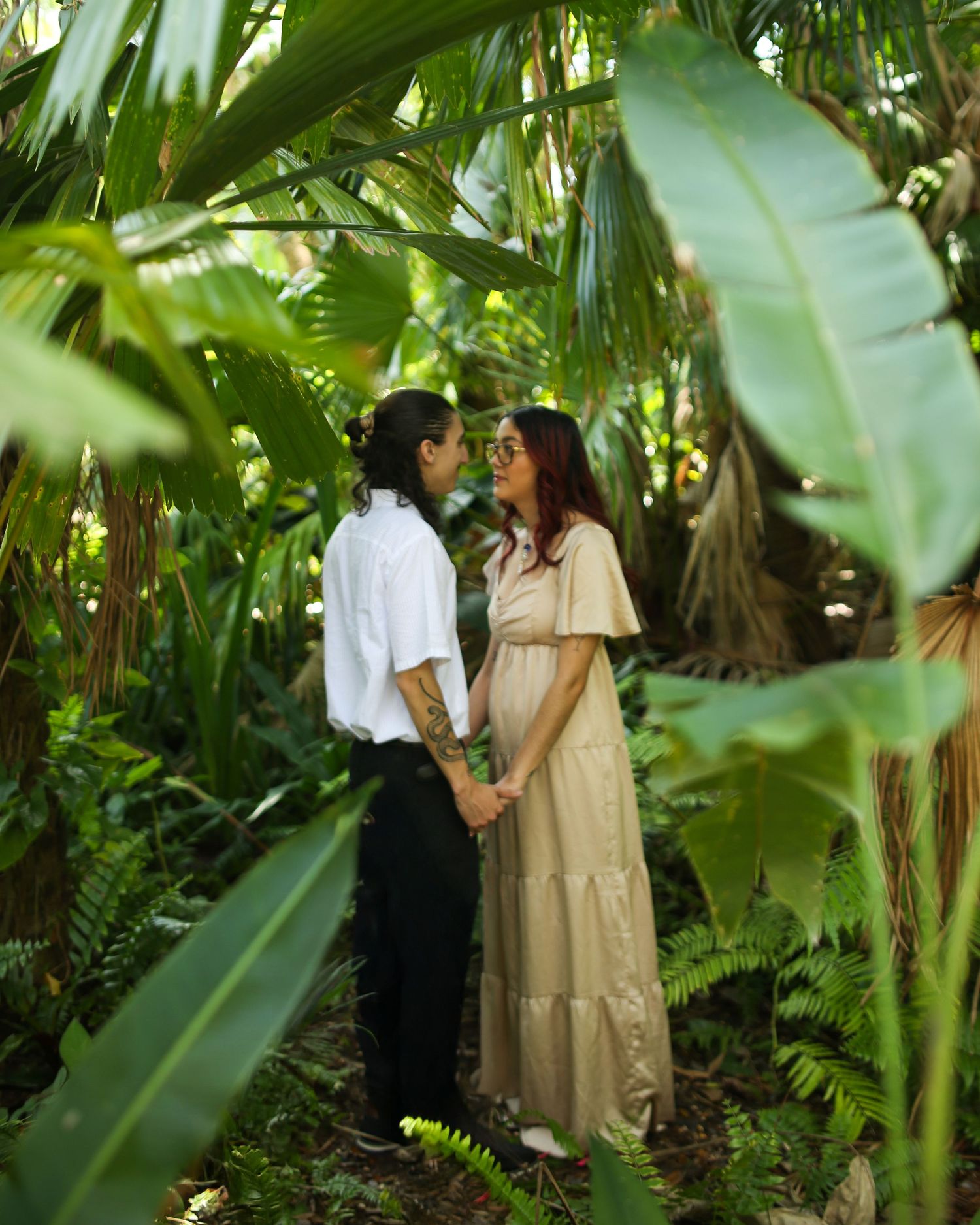 Couple sharing an intimate moment in a lush tropical garden setting with palm fronds and greenery at  Harry P. Leu Gardens in Florida.