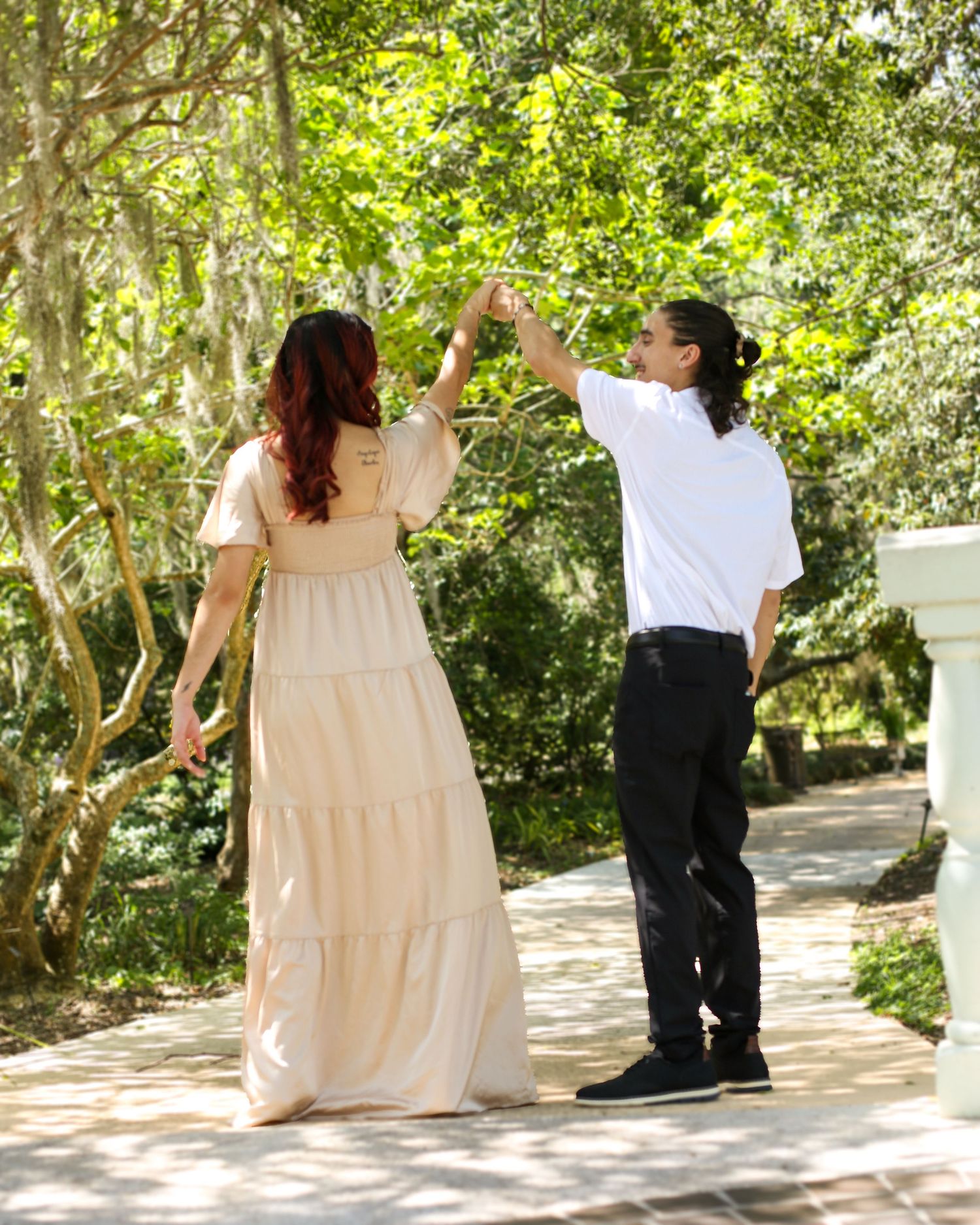 Dancing couple twirling on a sunlit garden path surrounded by trees at Harry P. Leu Gardens in Florida.