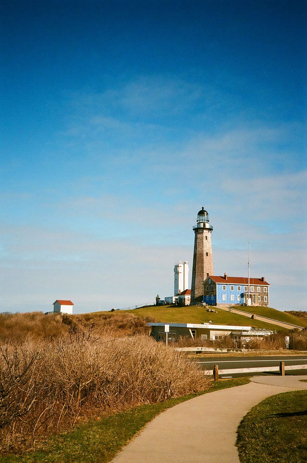 Historic Montauk Point lighthouse standing tall on a grassy hill with a winding pathway leading to its entrance.