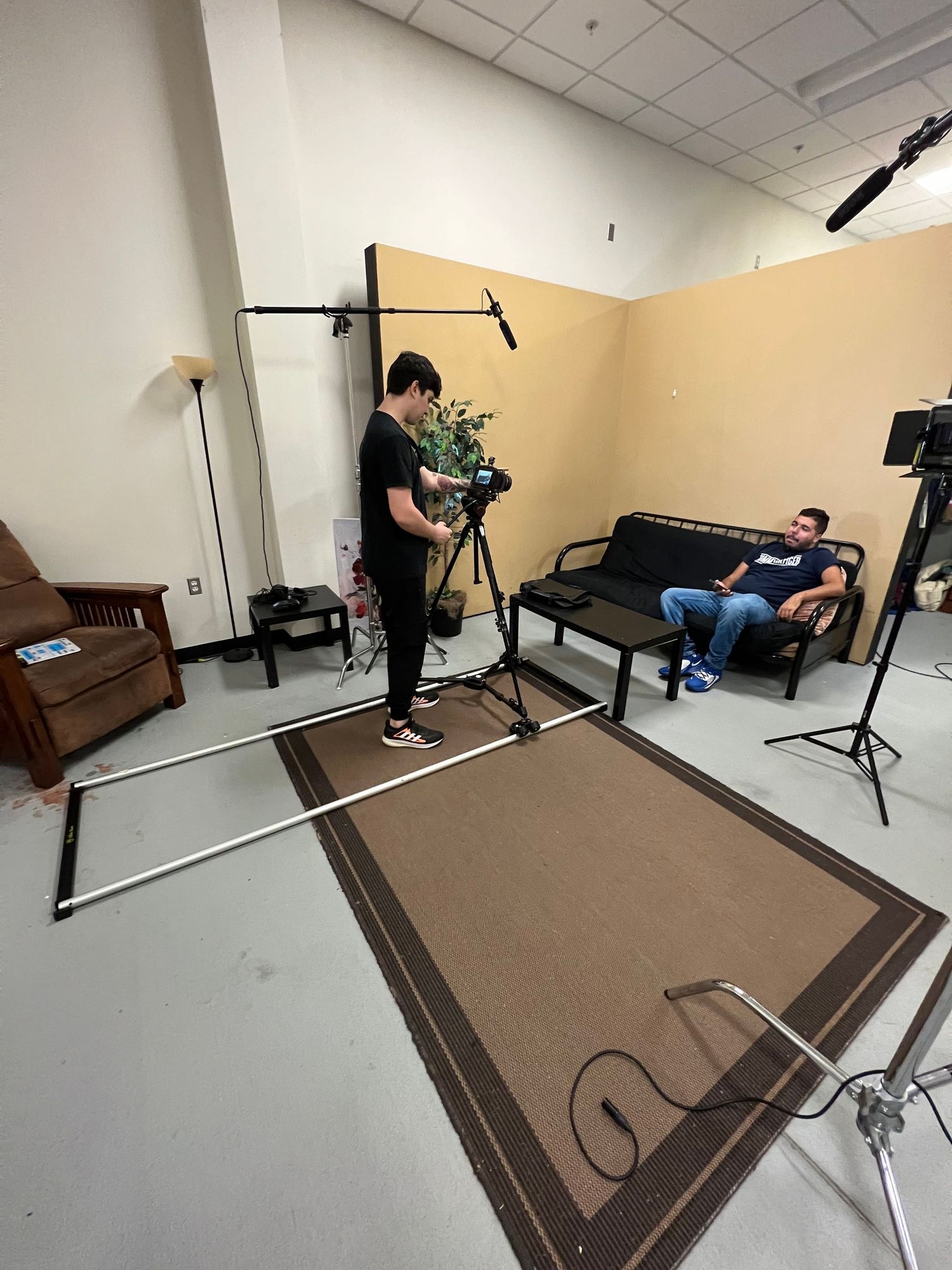 Behind the scenes of a short film production set with a camera, dolly, boom, and c-stand..