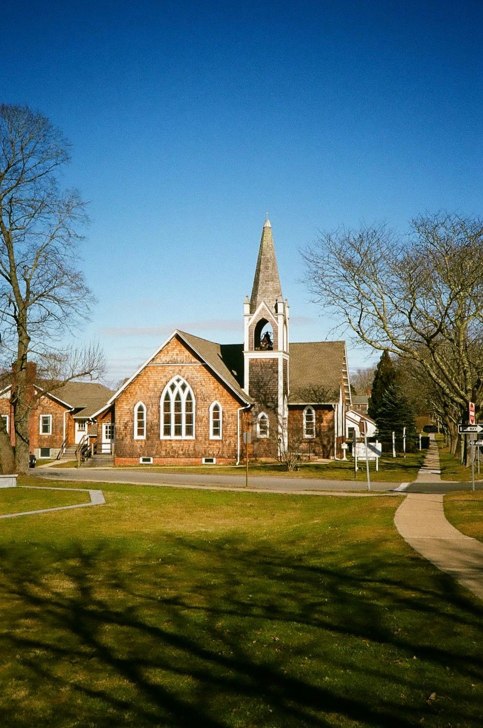 Traditional brick church with tall white spire and Gothic windows under clear blue sky in the Hamptons, NY.