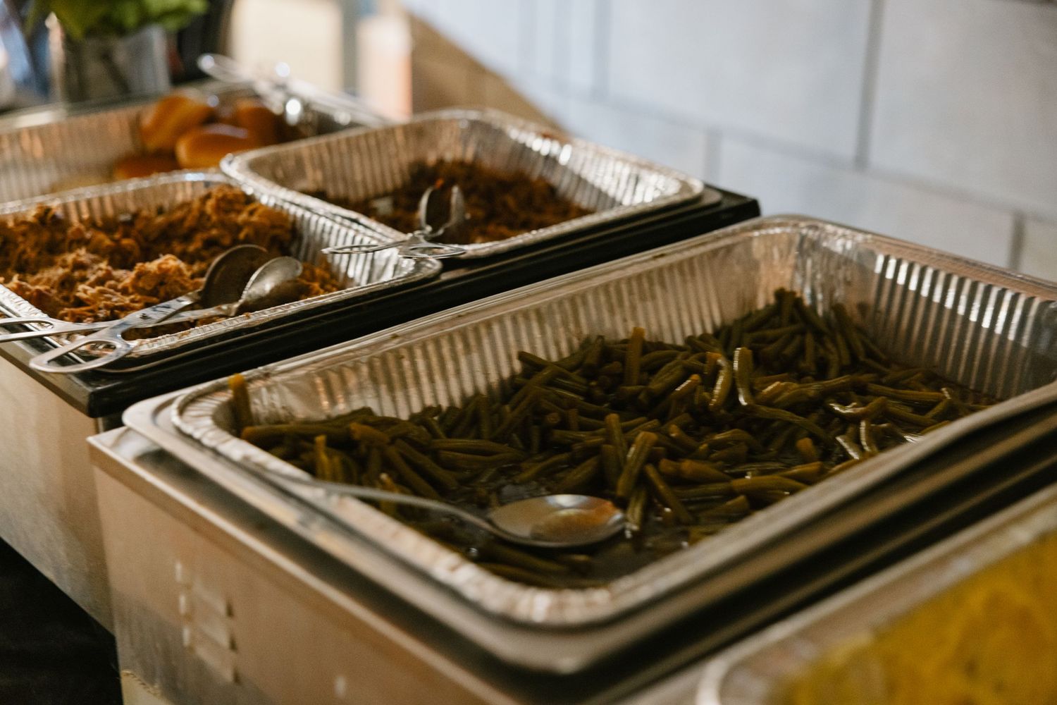 Multiple aluminum foil catering trays filled with barbecue and grilled food items arranged in a row.
