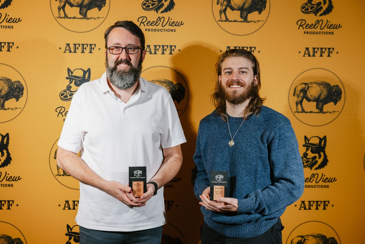 Two award winners holding trophies at an event with AFFF branded backdrop.
