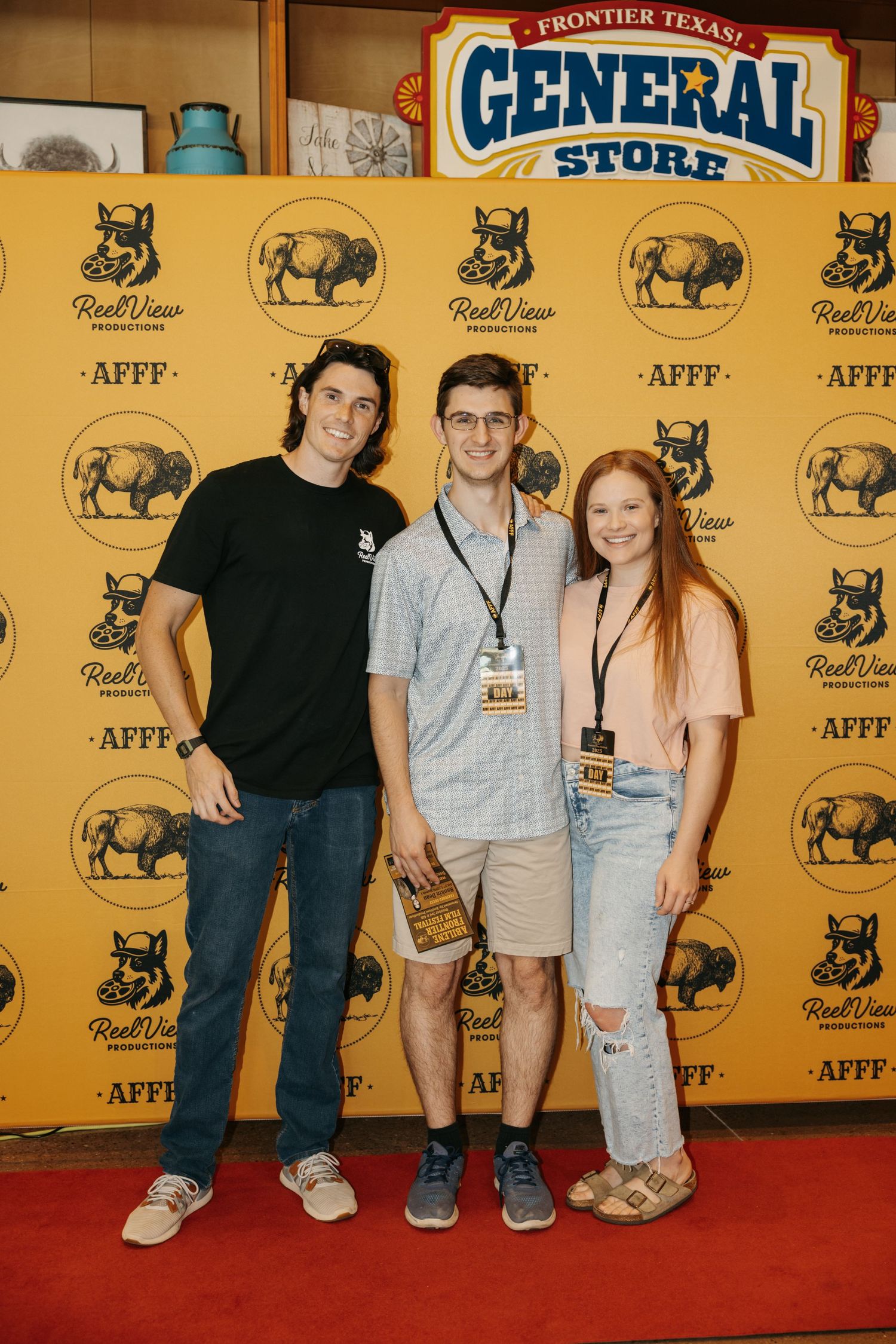 Three people pose together on a red carpet against a yellow backdrop with Frontier Texas General Store branding.