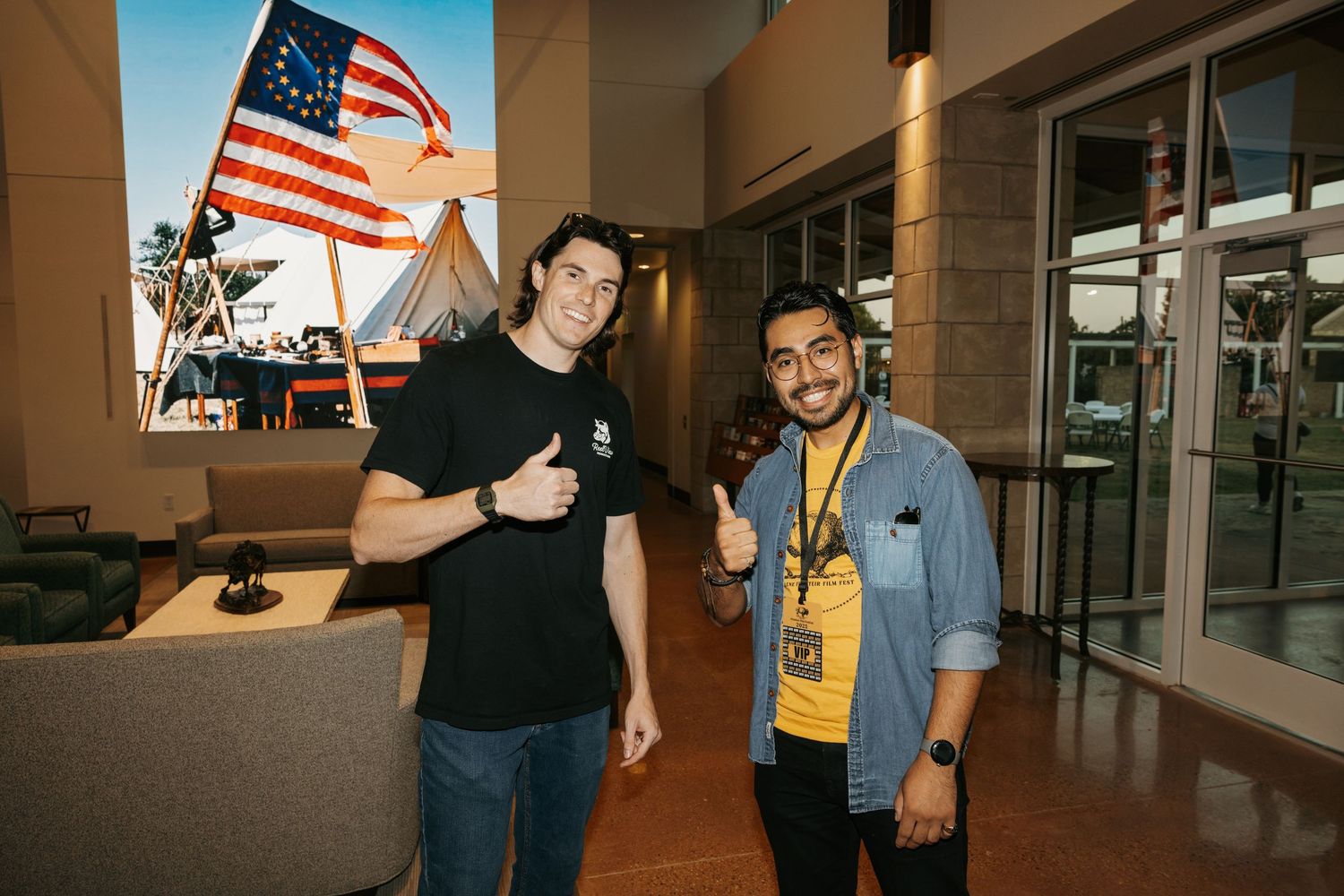 Two people posing together in front of an American flag inside a building.