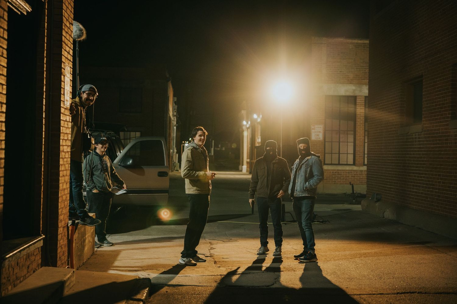 Four people standing on a dimly lit urban street at night with a bright street lamp glowing behind them.