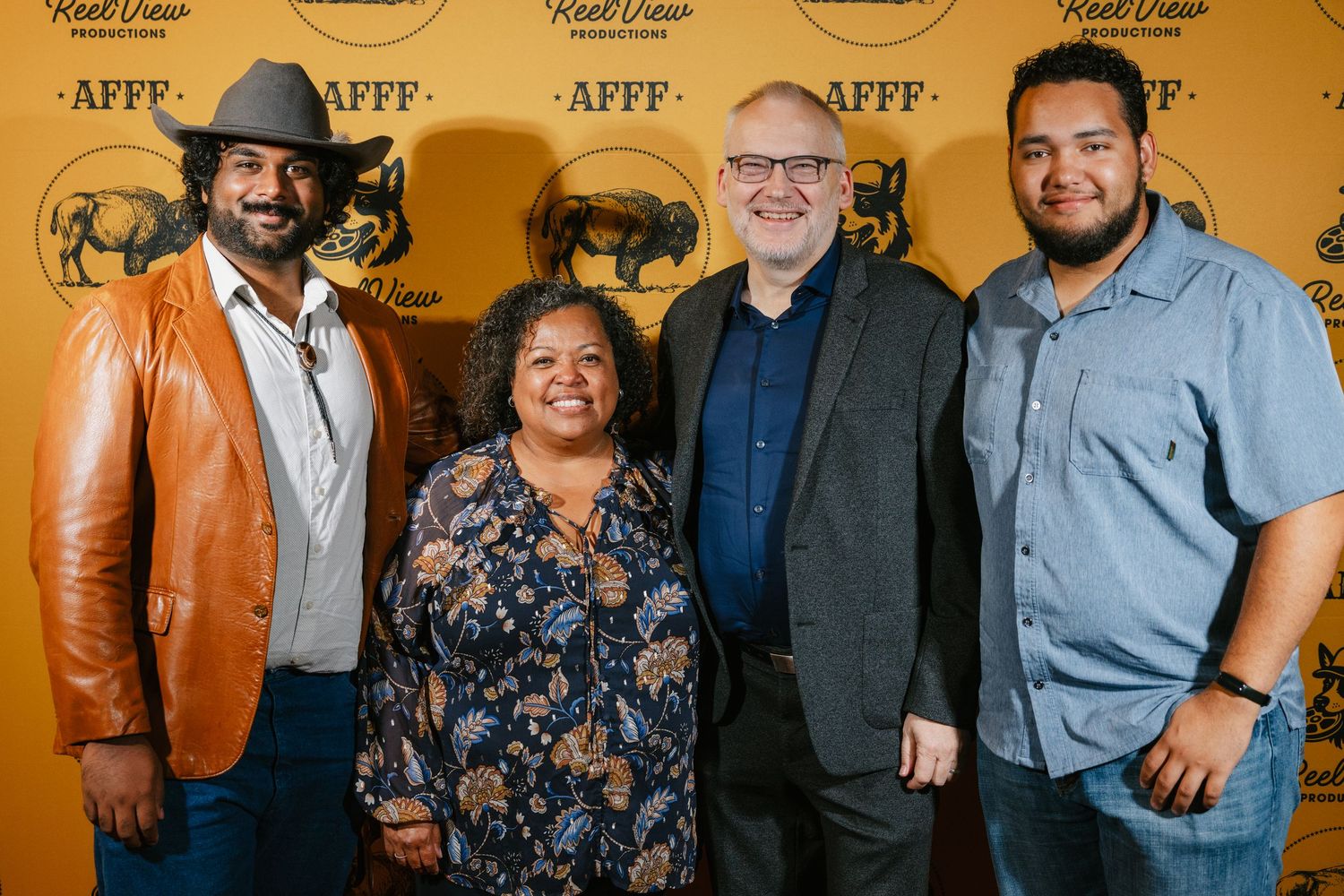 Group portrait of people standing together against a warm golden-toned background.