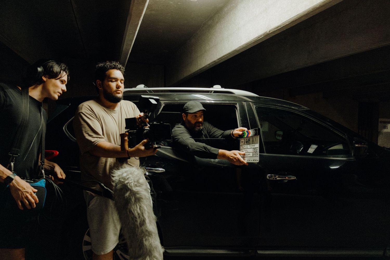Film crew shooting a scene with a black SUV in a parking garage, with cameraman and director collaborating.