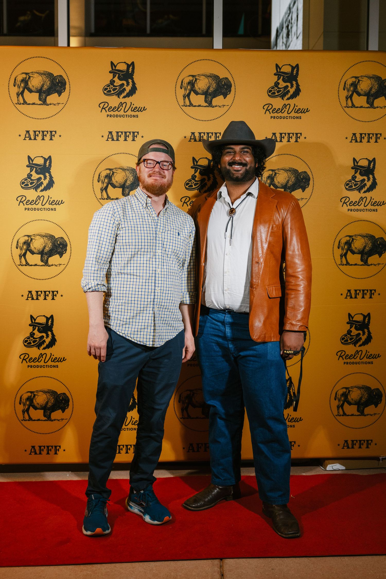 People in western attire pose on a red carpet against a yellow backdrop with buffalo logos.