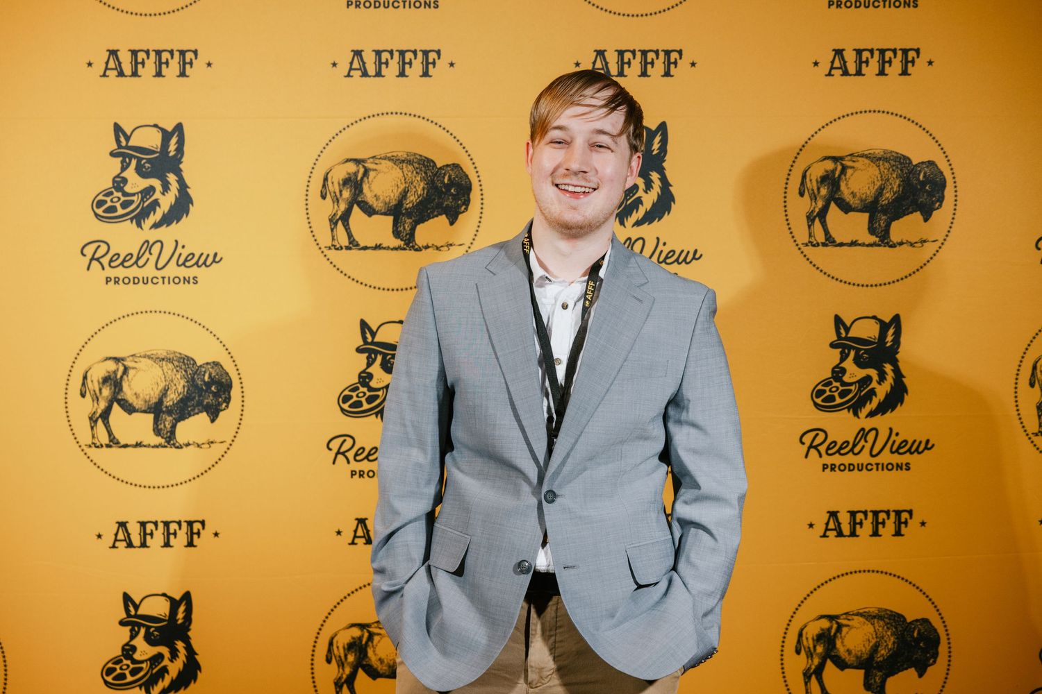 Person in gray suit poses against yellow backdrop with repeating bull logo pattern at press event.