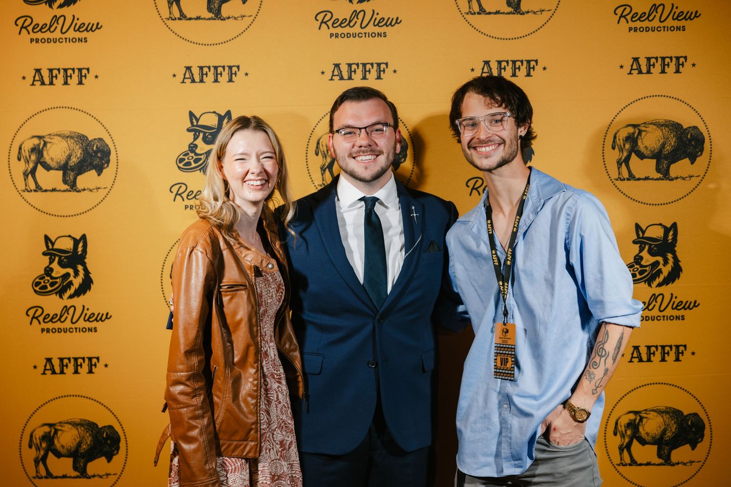 Three people pose together against a yellow backdrop with buffalo logos at a film festival event.