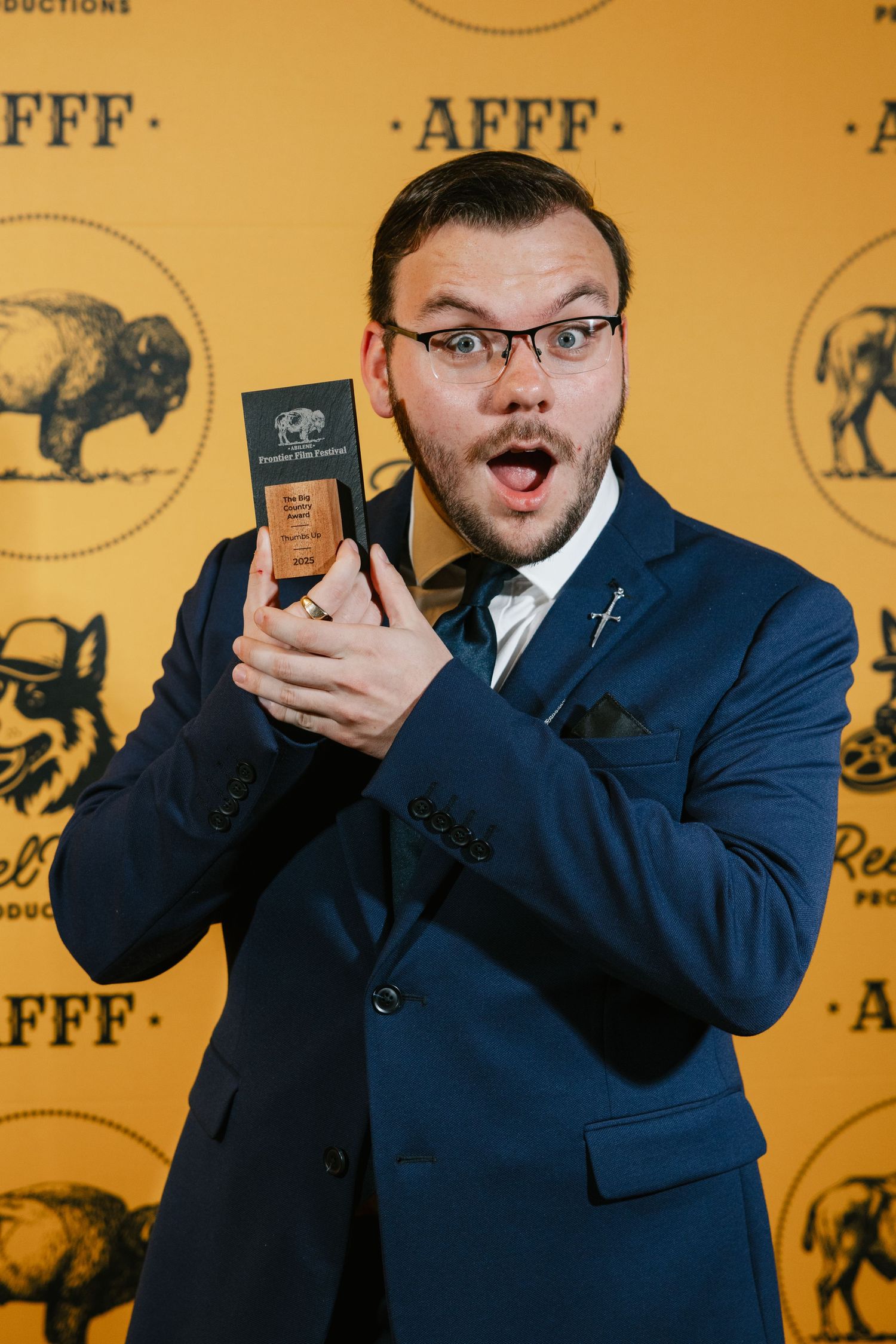 Person in blue suit reacts with surprise while holding small object against yellow background with FFF text.