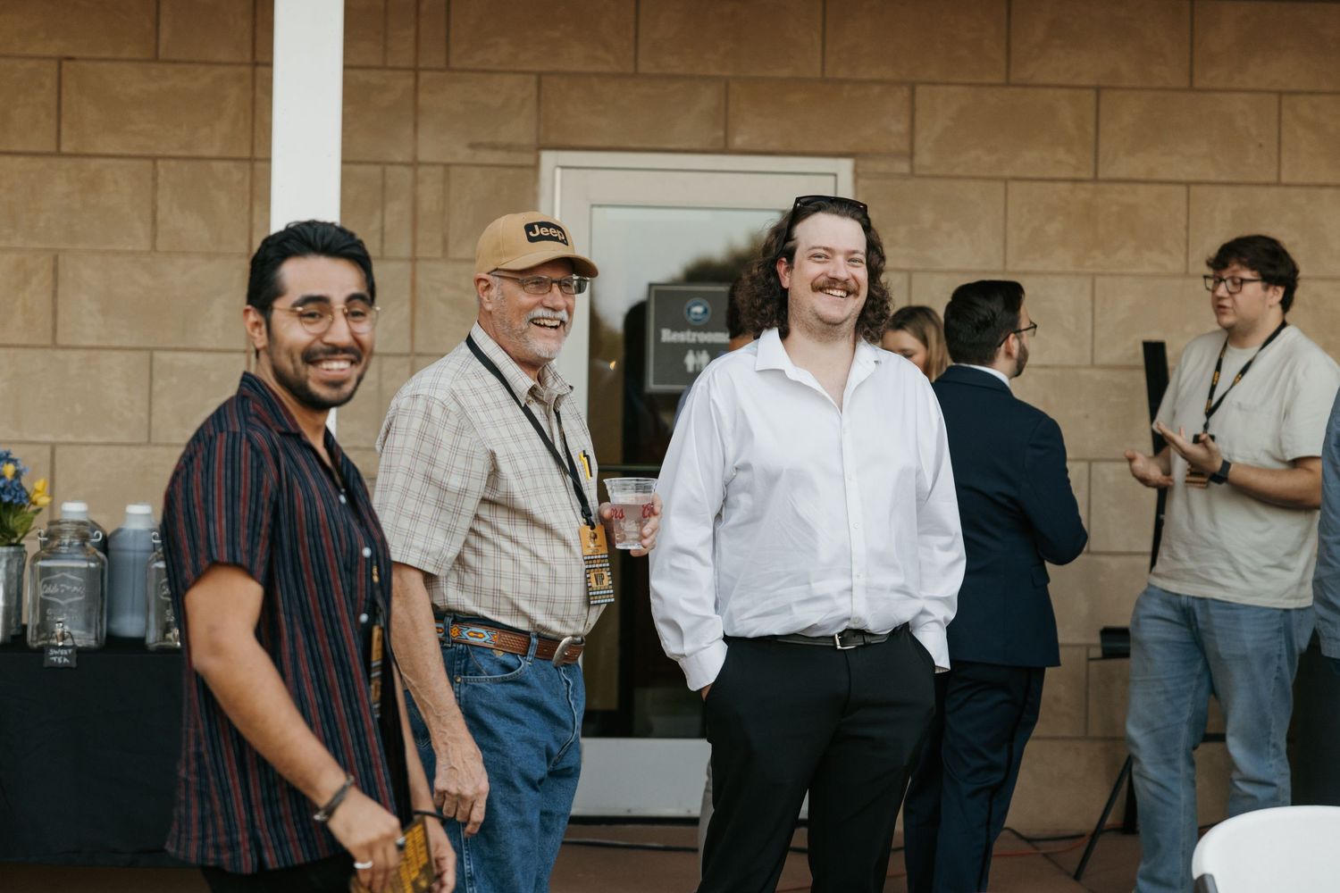 People gathered at an indoor event space with beige brick walls and white doors in the background.