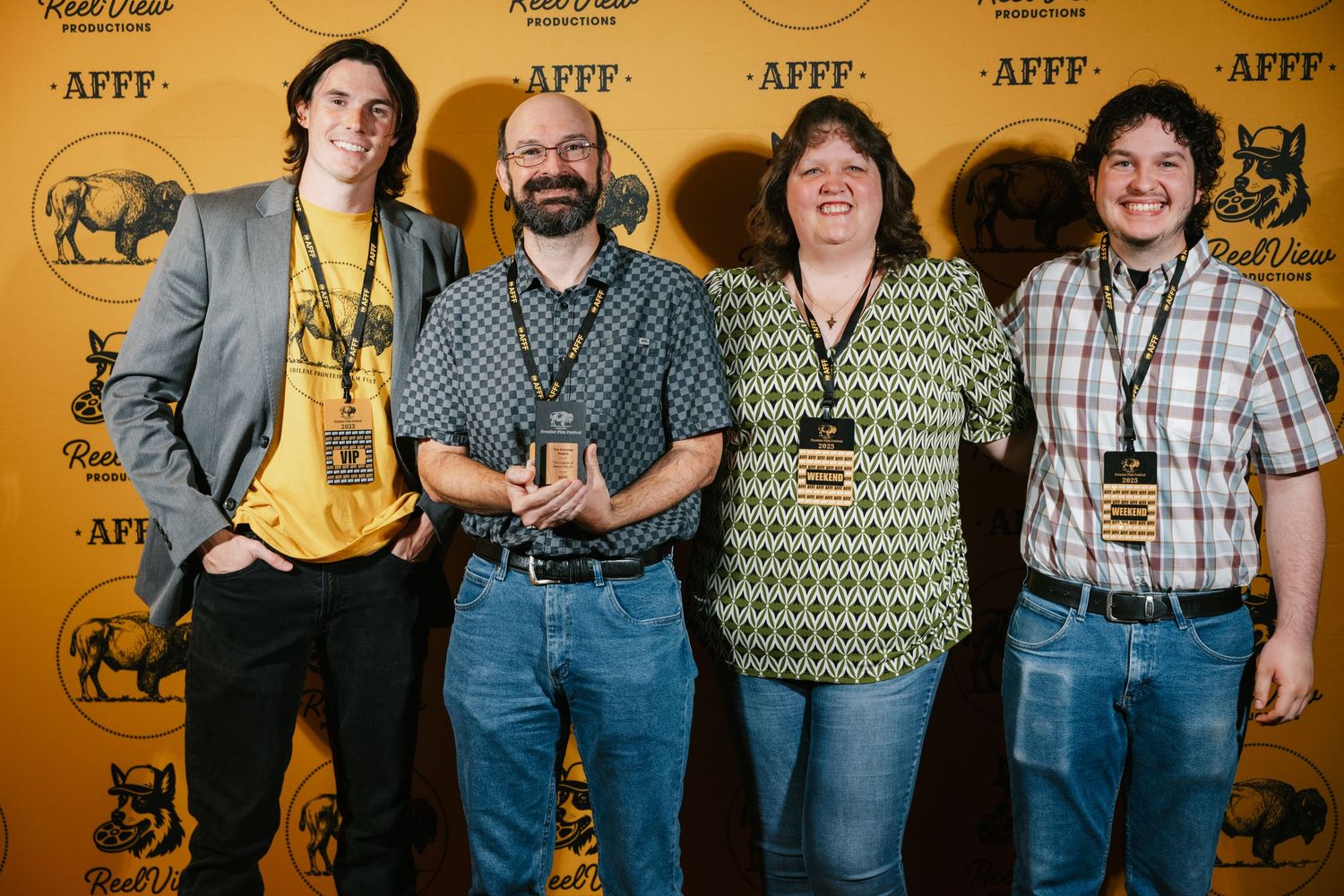 A group of people standing together in casual attire against a golden-colored wall with animal artwork.