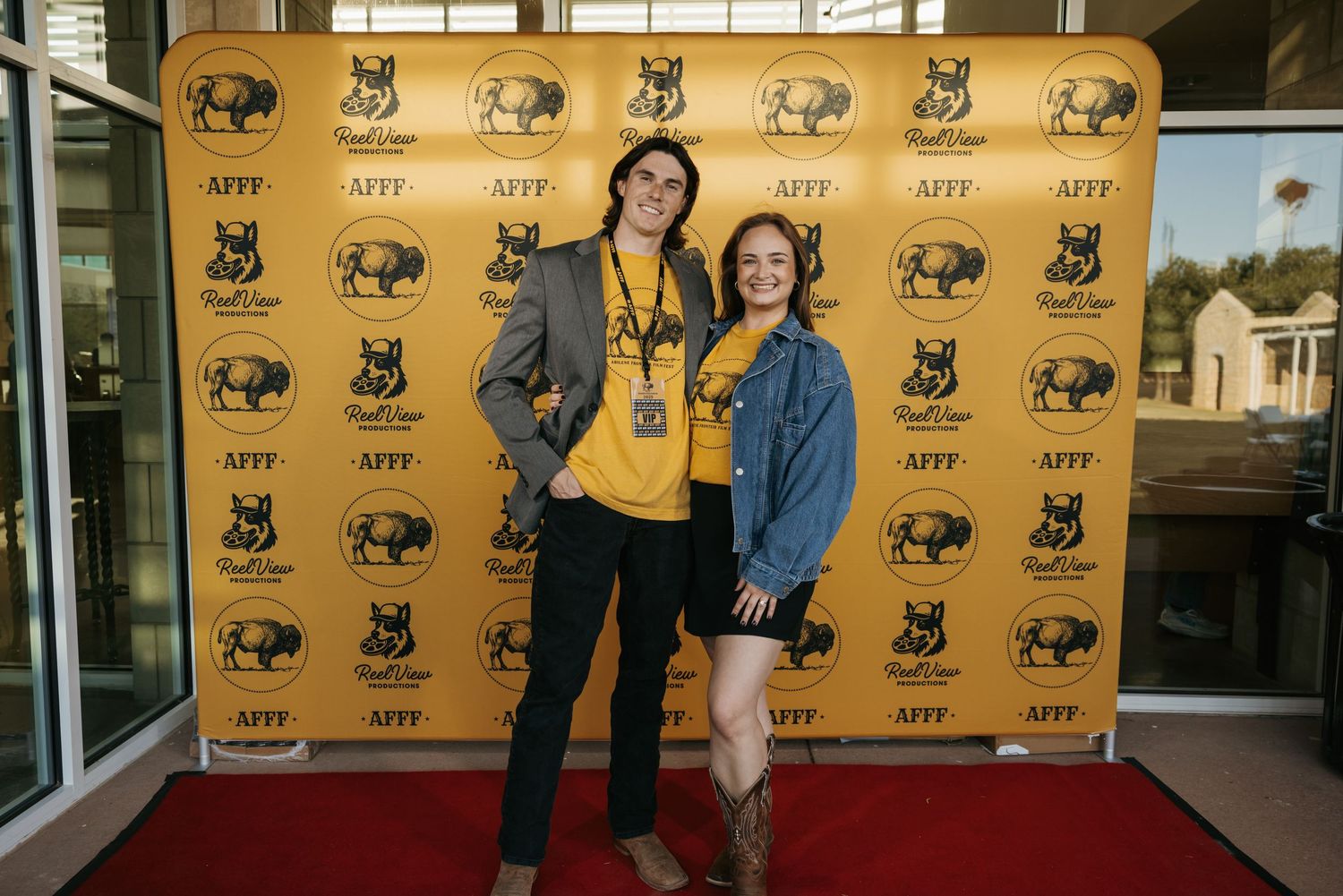 People pose on a red carpet with yellow step-and-repeat backdrop featuring buffalo logos at an event.