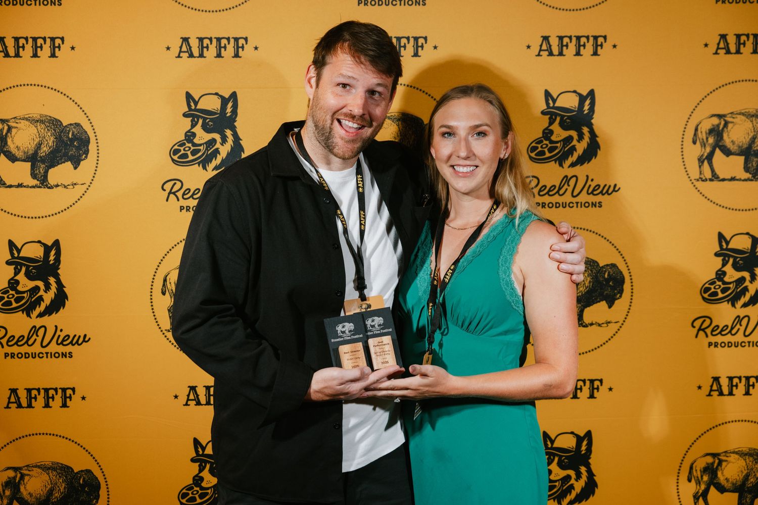 A couple poses together at an event against a yellow backdrop with repeating AFFF text and animal logos.