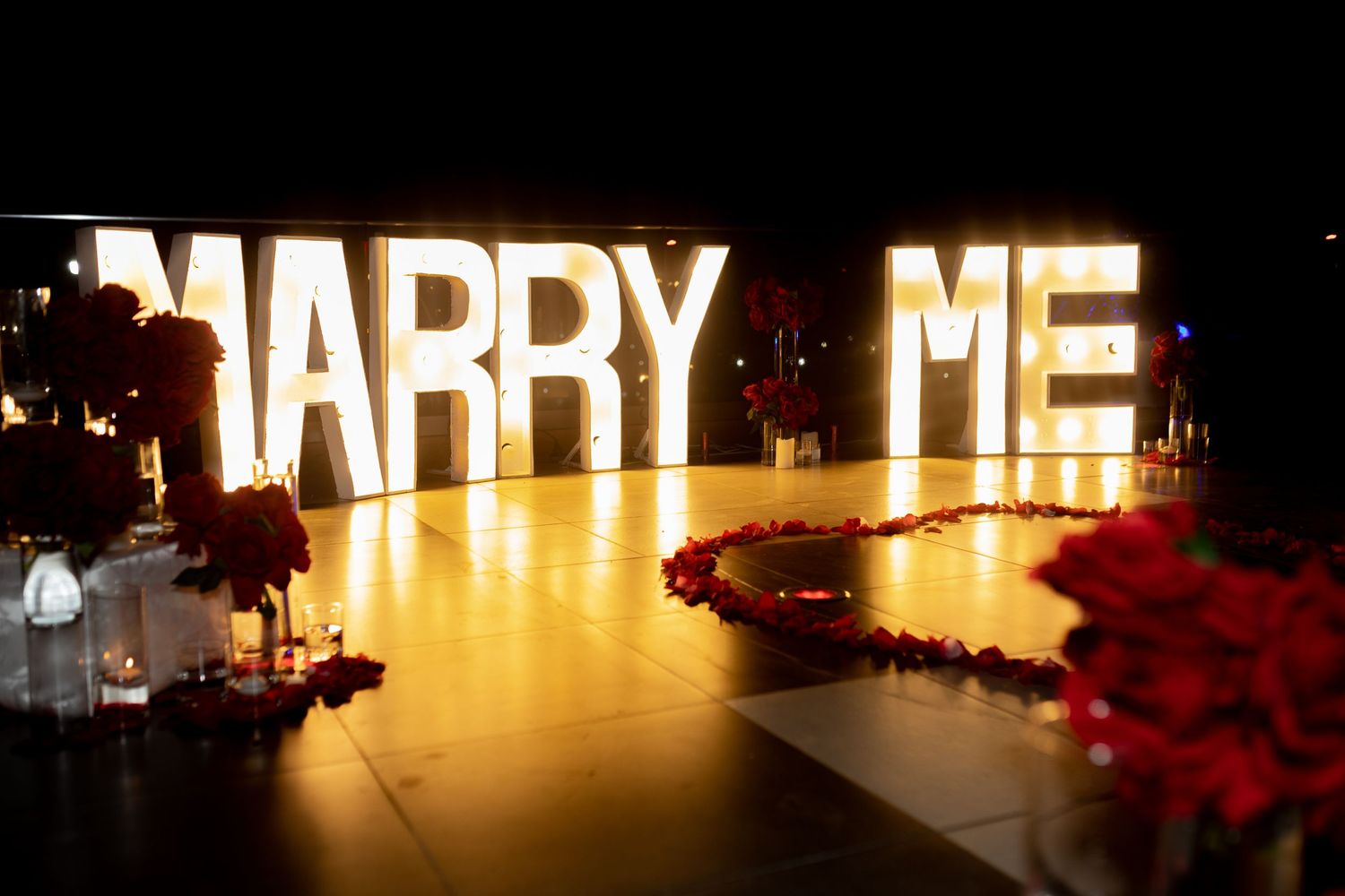 Proposal setup with candles, flowers, and “Marry Me” sign