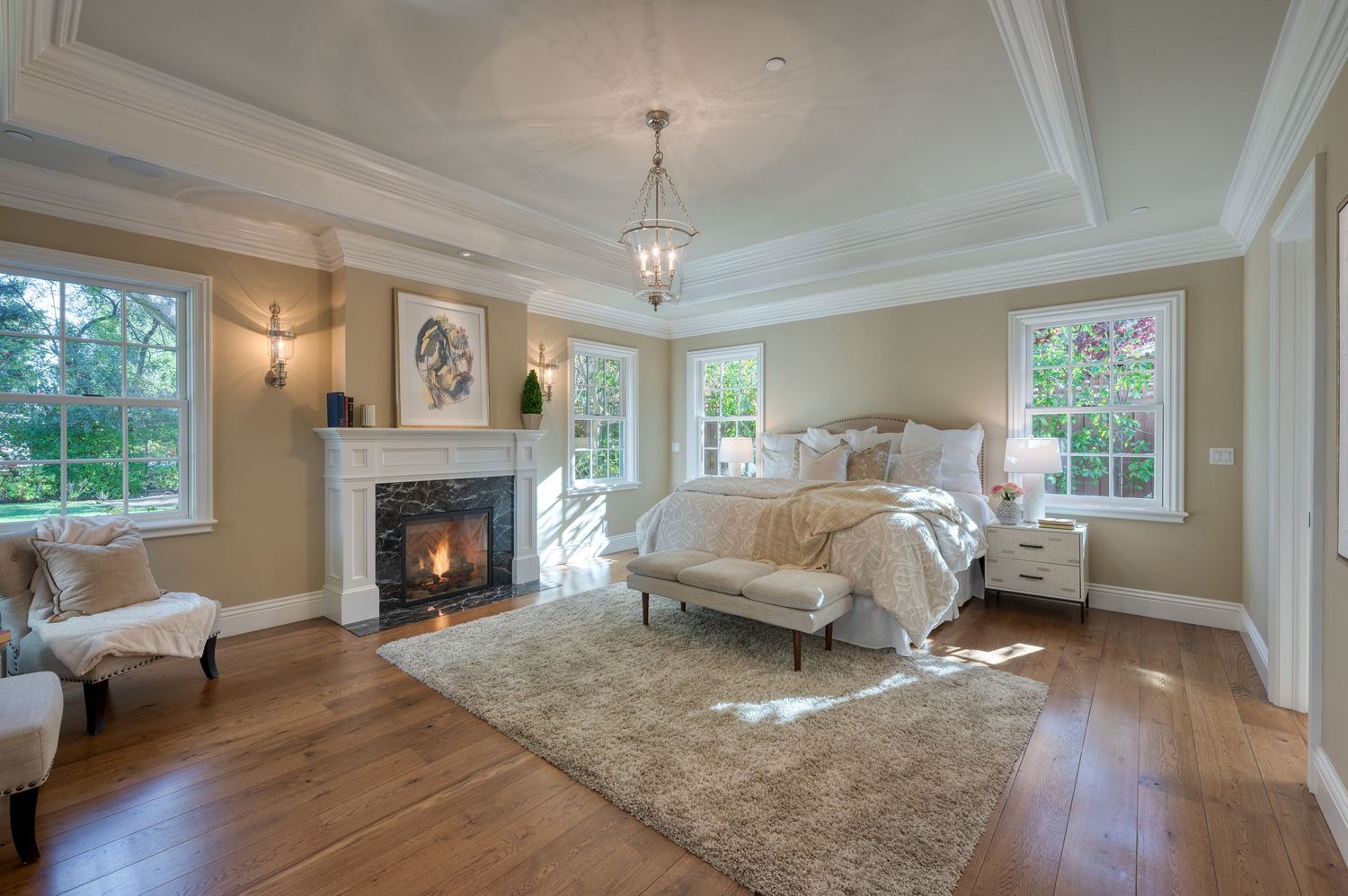 Master bedroom with fireplace, crown molding, and large windows overlooking garden views.