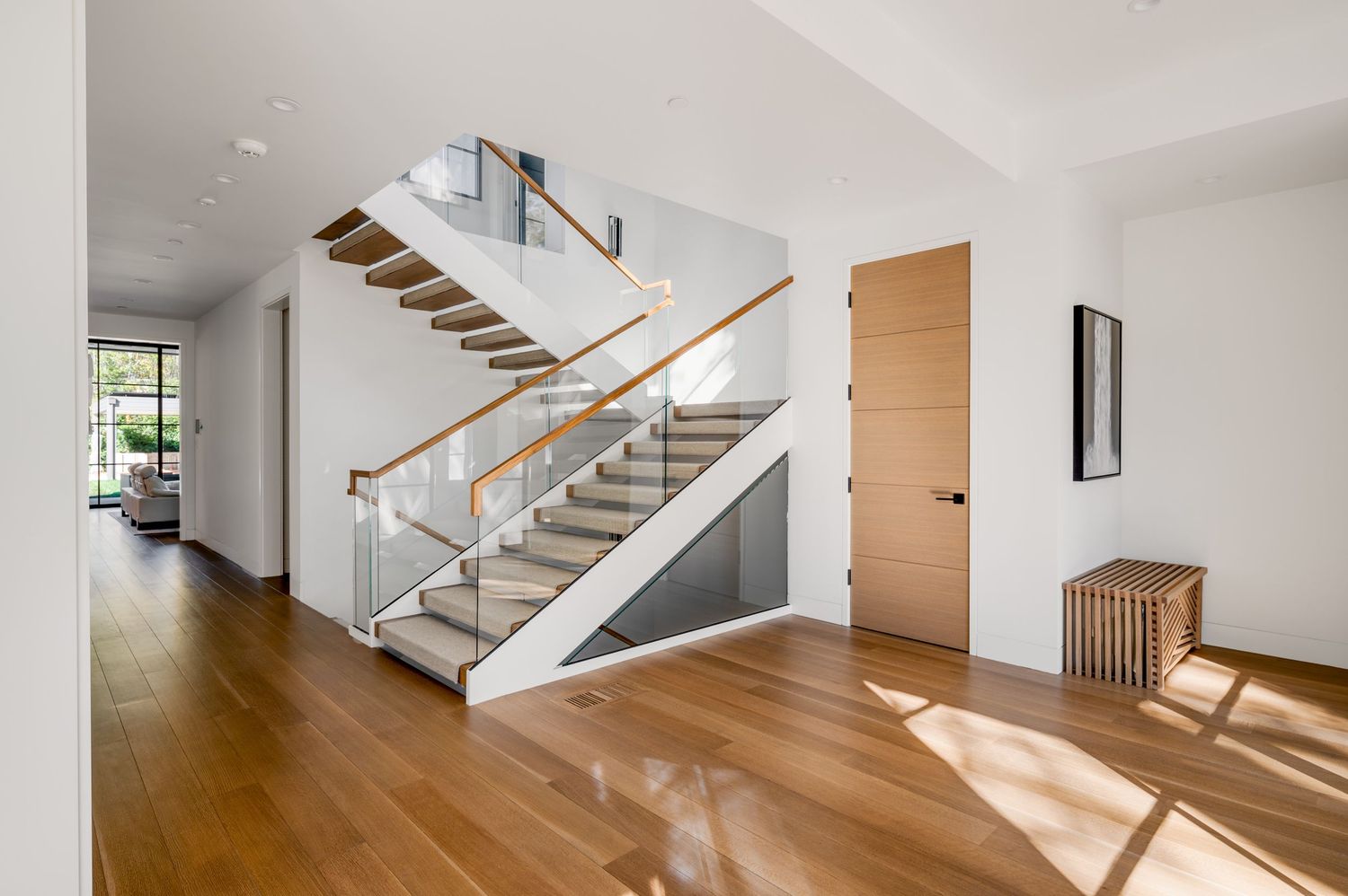 Modern staircase with glass railings and wooden treads in a sunlit contemporary home.