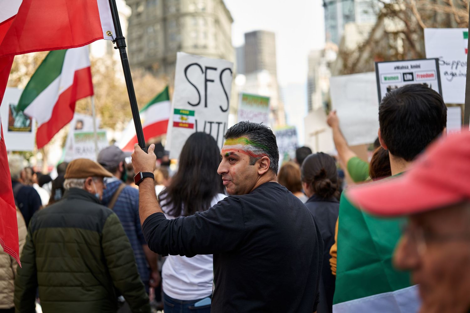 Protesters at a rally holding flags and signs in an urban setting.