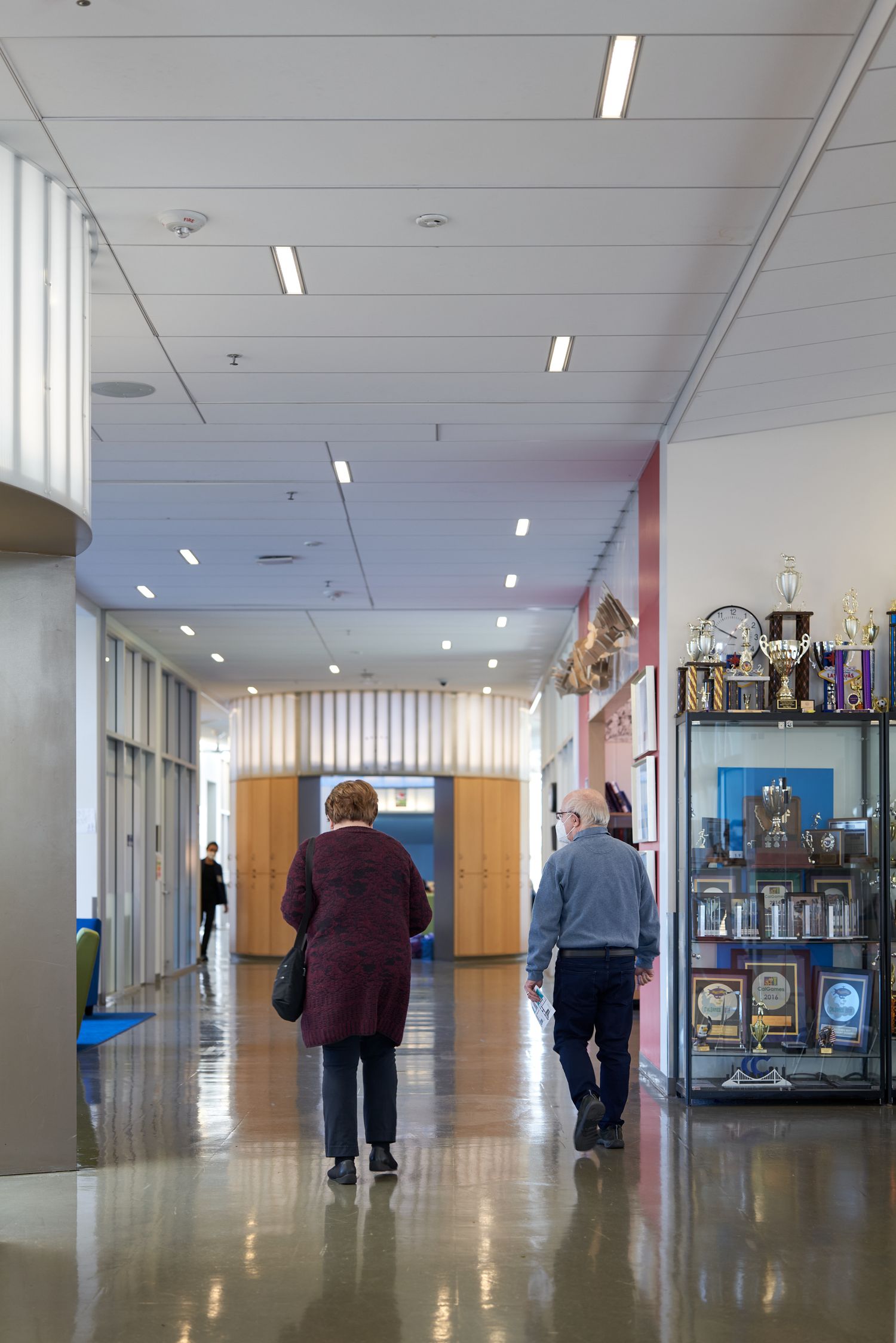 People walking down a bright institutional hallway with vending machines along the wall.